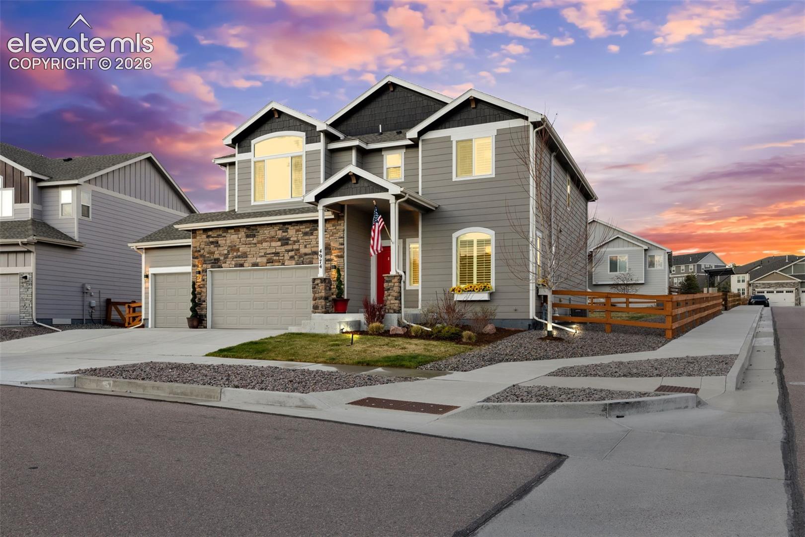 Two-story gray house with stone accents, double garage, and red front door at sunset.