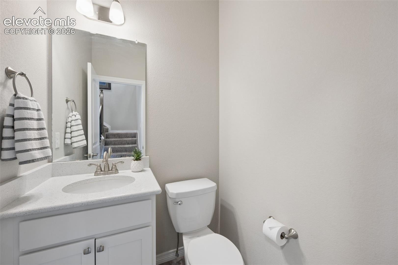 Bathroom with white vanity, oval sink, large mirror, and toilet beside a reflected stairway.