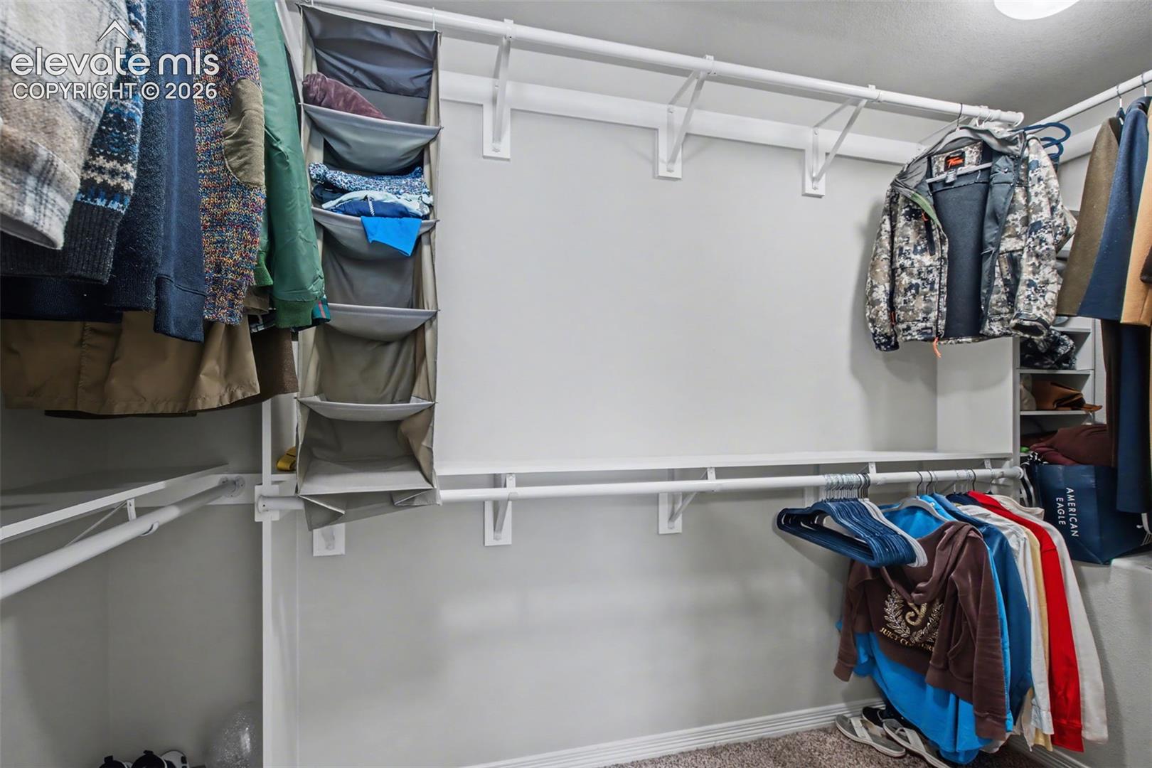 Walk-in closet with white shelving, fabric organizers, and clothes hanging along the walls.