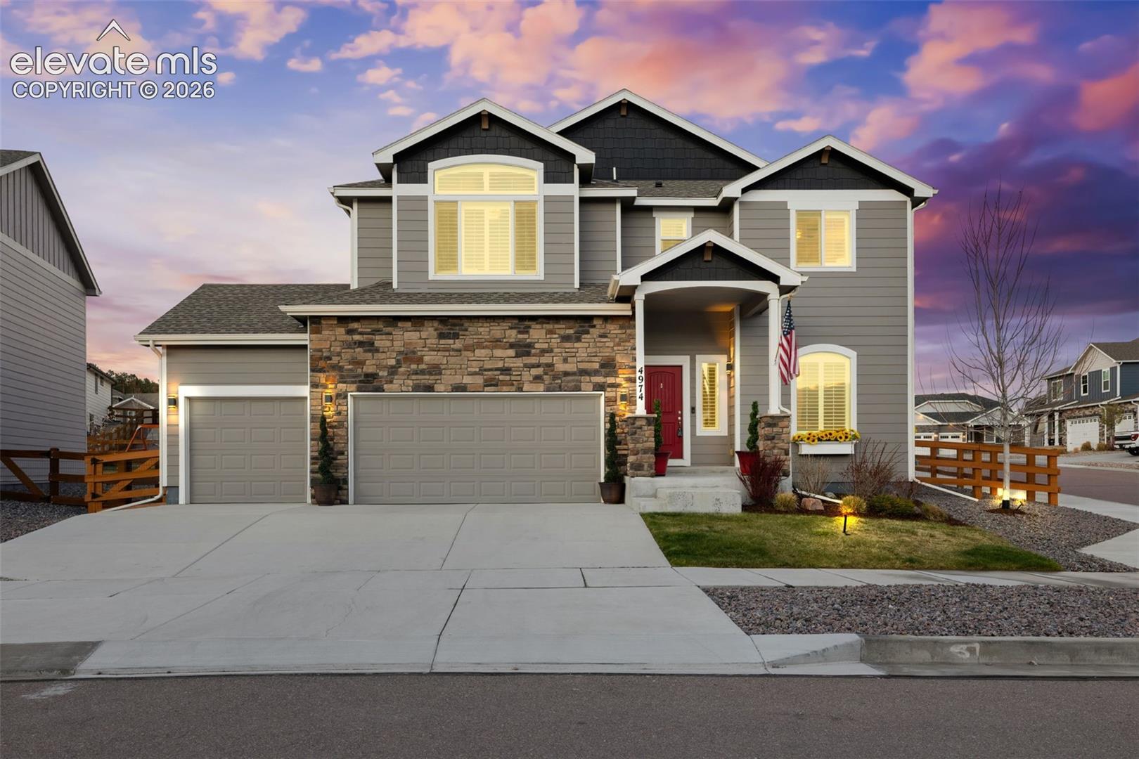 Two-story gray house with a stone facade, double garage, and covered entry at dusk.