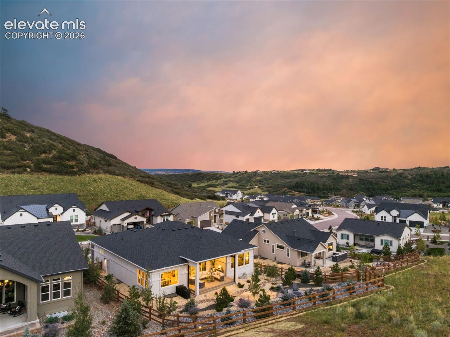 Aerial view of homes in a hillside neighborhood beneath a pink-orange sunset sky.