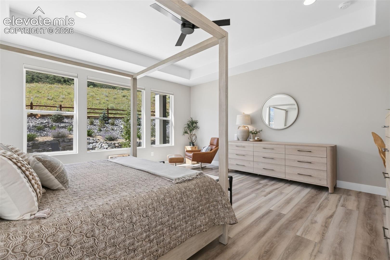 Staged bedroom with a four-poster bed, tall hillside-facing windows, and a leather reading chair.