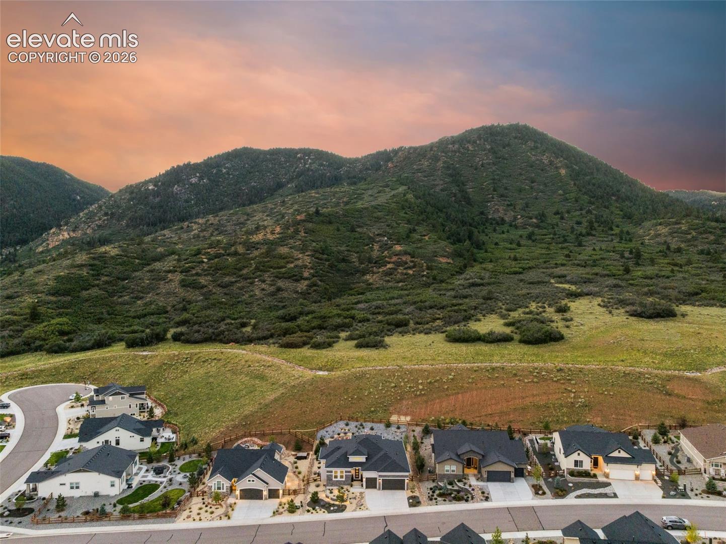 Aerial view of homes below a scrub-covered mountain beneath a pink dusk sky.