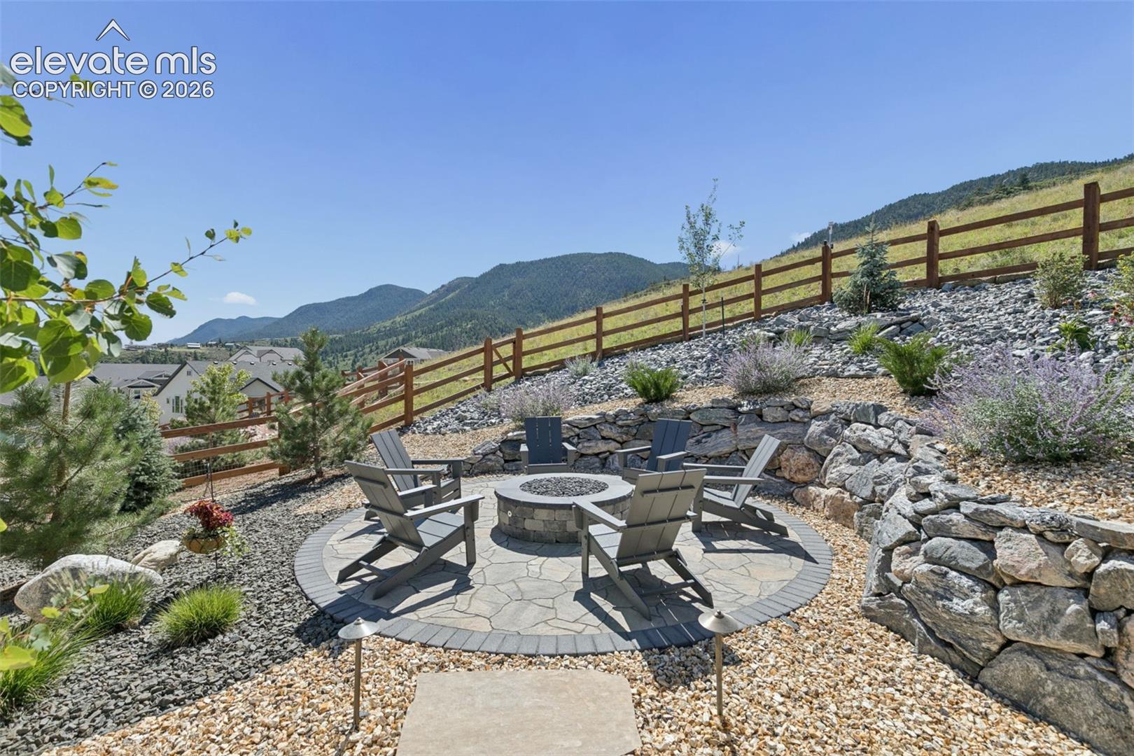Stone patio with fire pit and Adirondack chairs overlooking forested mountains.