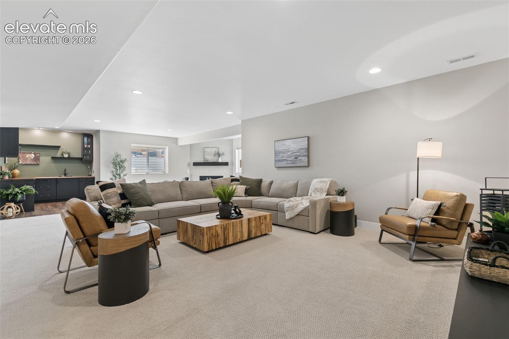 Staged living room with a large sectional, leather armchairs, and an open kitchen.