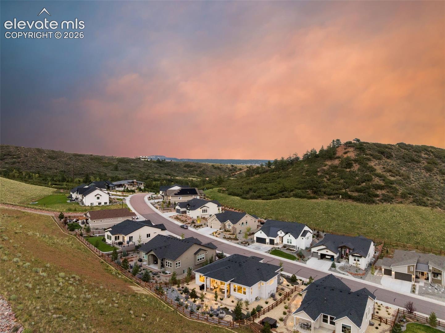 Aerial view of homes along a curving street beneath a vivid orange dusk sky.