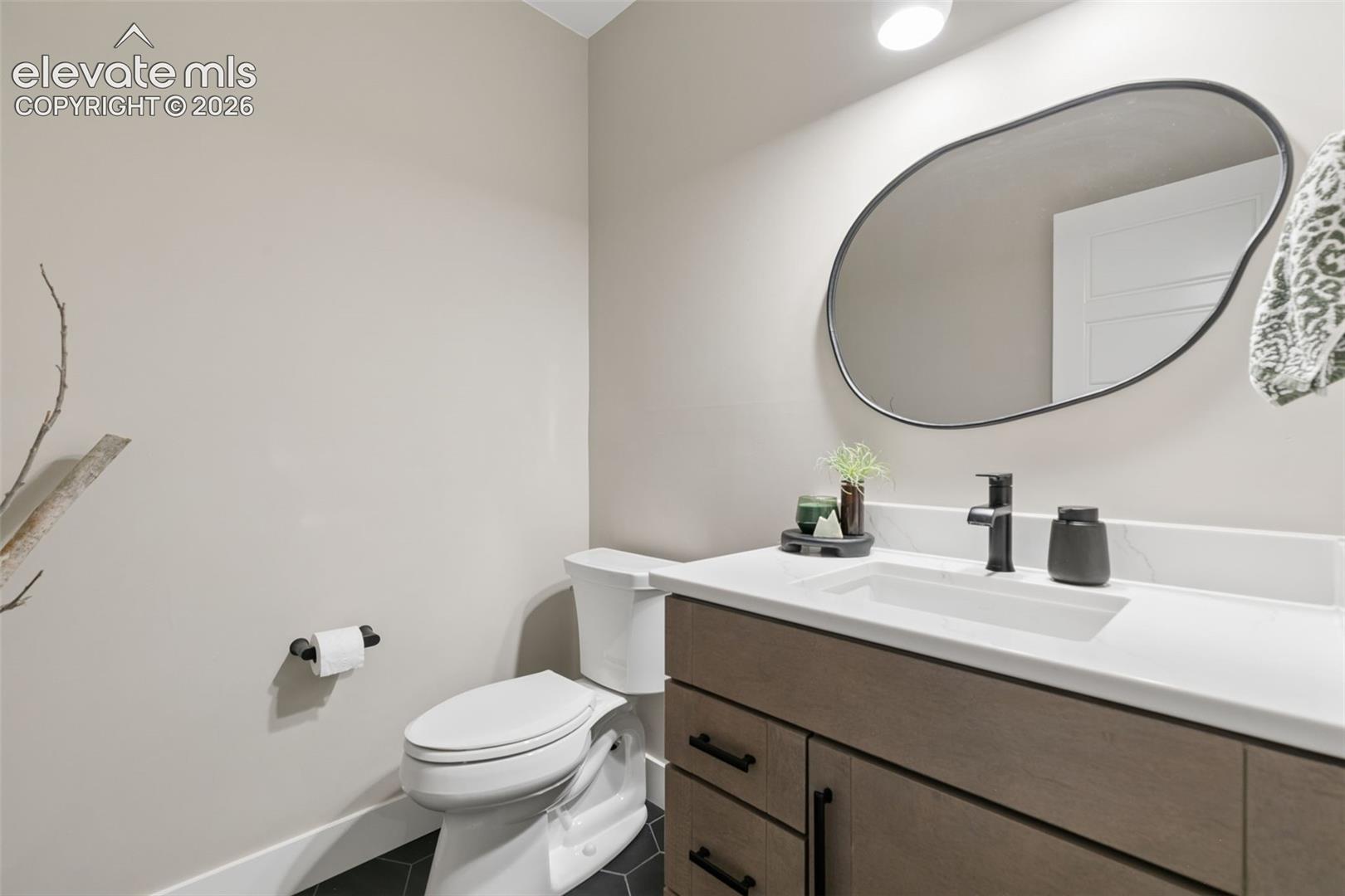 Modern bathroom with a wood-tone vanity, large oval mirror, and dark geometric floor tile.