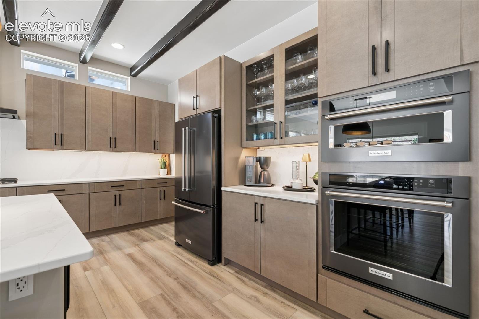 Modern kitchen with taupe cabinets, glass-front cupboards, and stainless steel wall ovens.