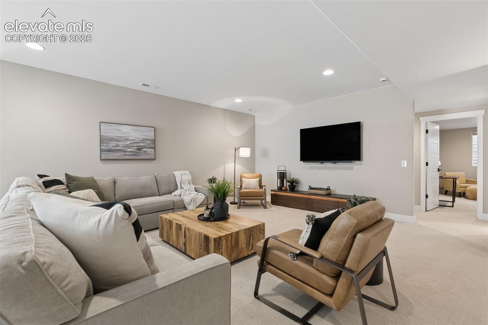 Staged living room with a gray sectional, wood coffee table, and wall-mounted television.