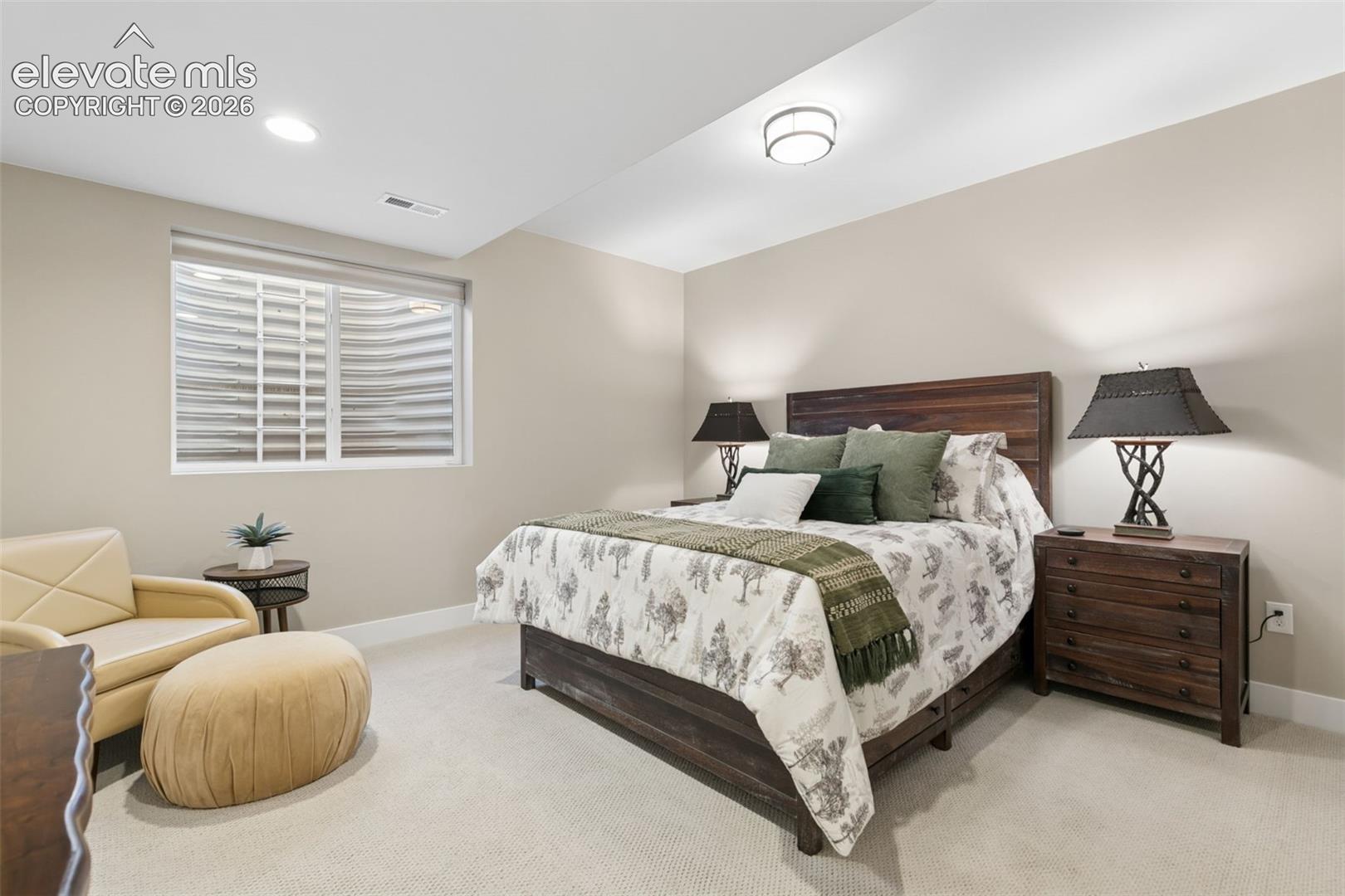 Furnished bedroom with a dark wood bed, patterned bedding, green accents, and a cream armchair.
