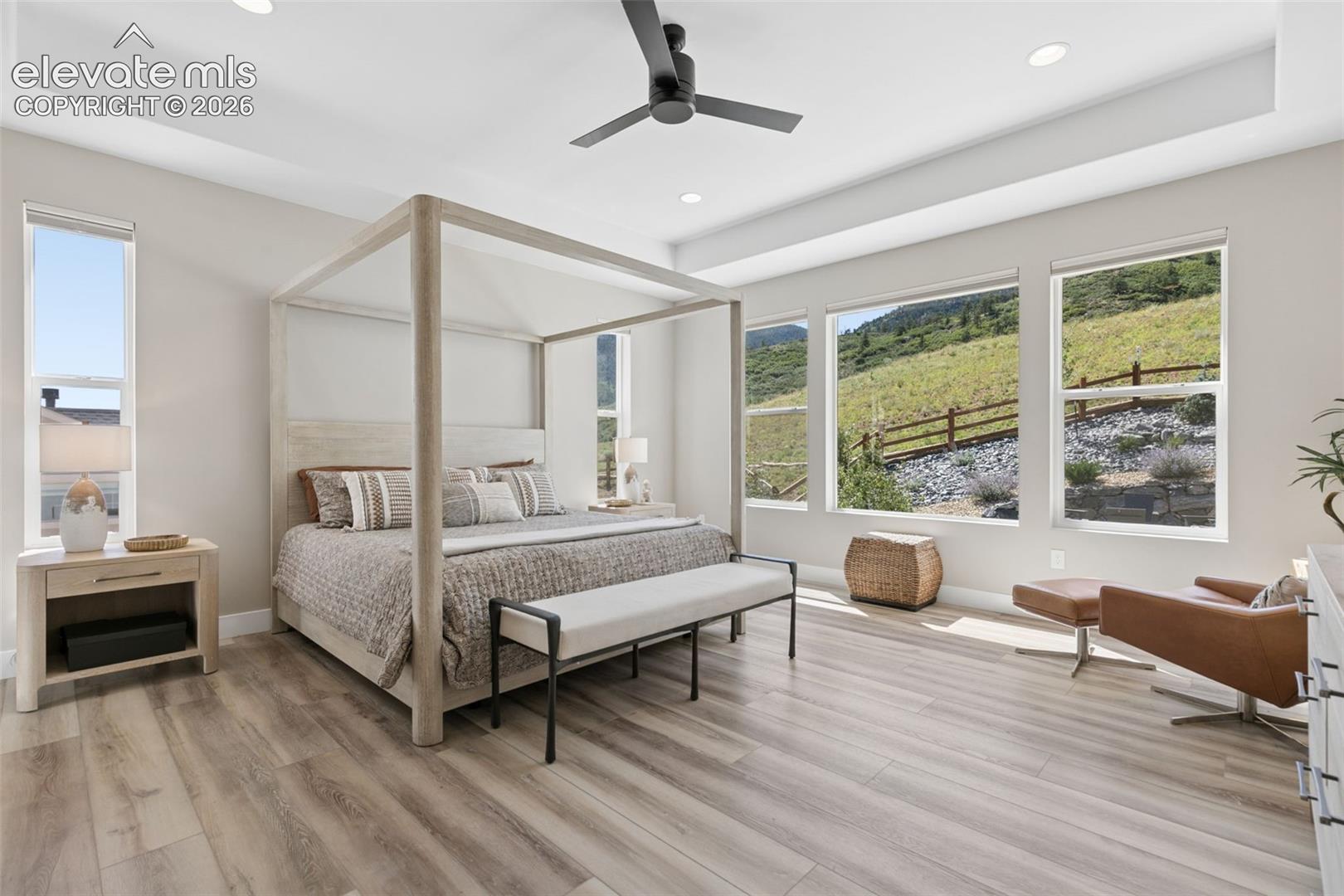 Furnished bedroom with a light wood canopy bed and large windows overlooking a green hillside.