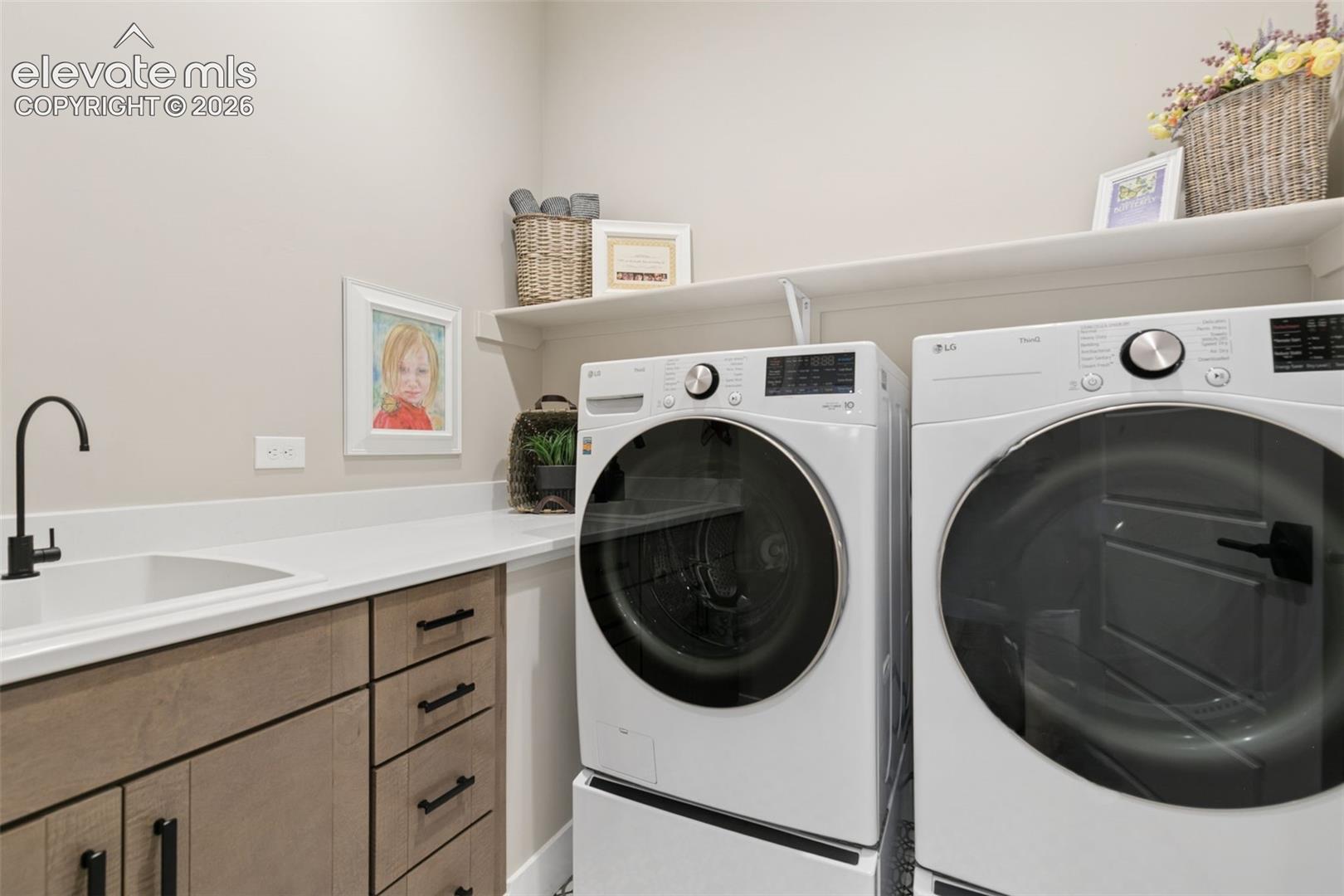 Laundry room with front-loading washer and dryer beside a utility sink and wood-tone cabinets.