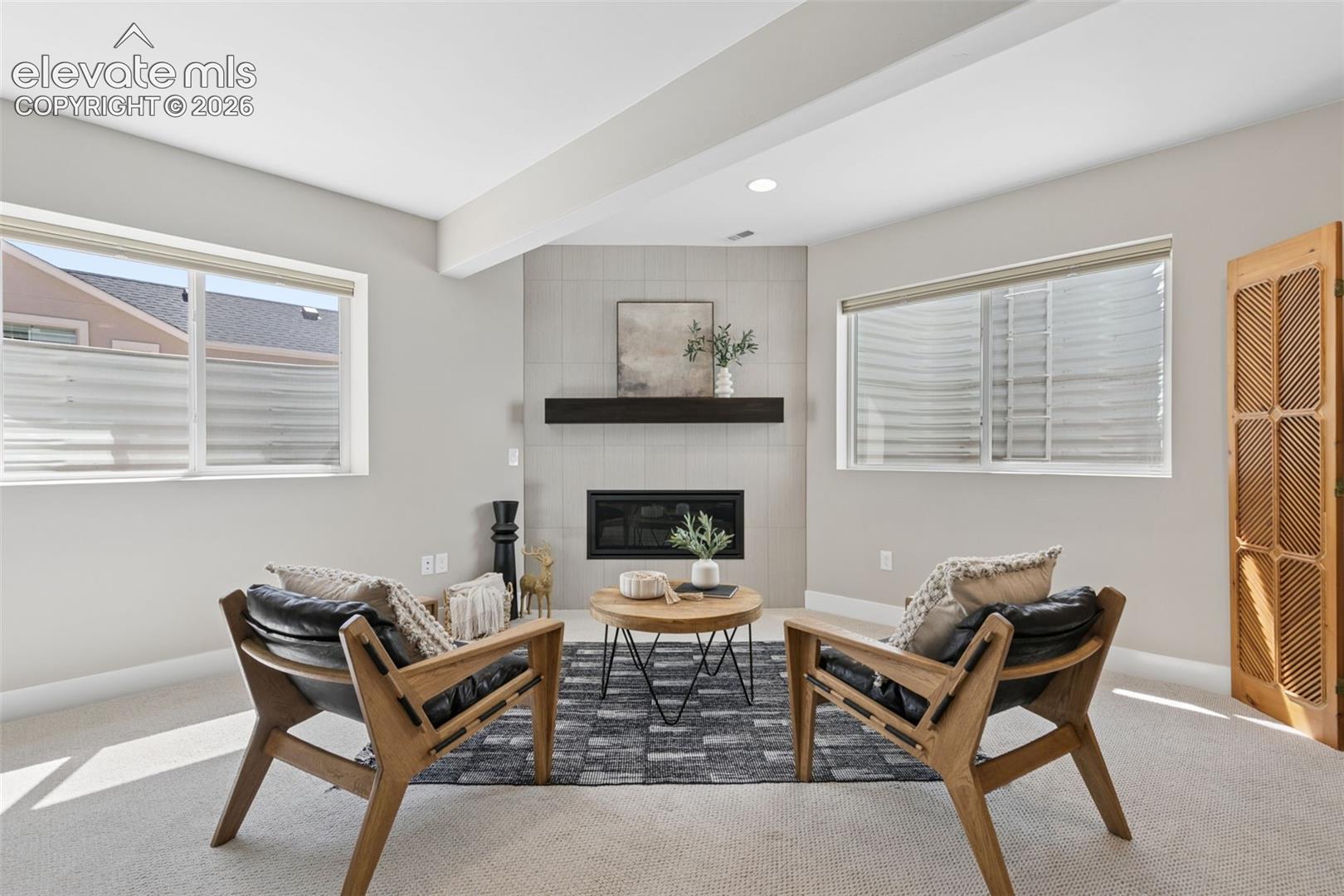 Staged living room with a tiled fireplace, floating mantel, and two wooden lounge chairs.