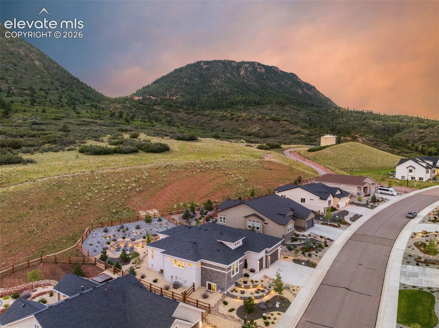 Aerial view of homes along a curving street below a mountain at sunset.