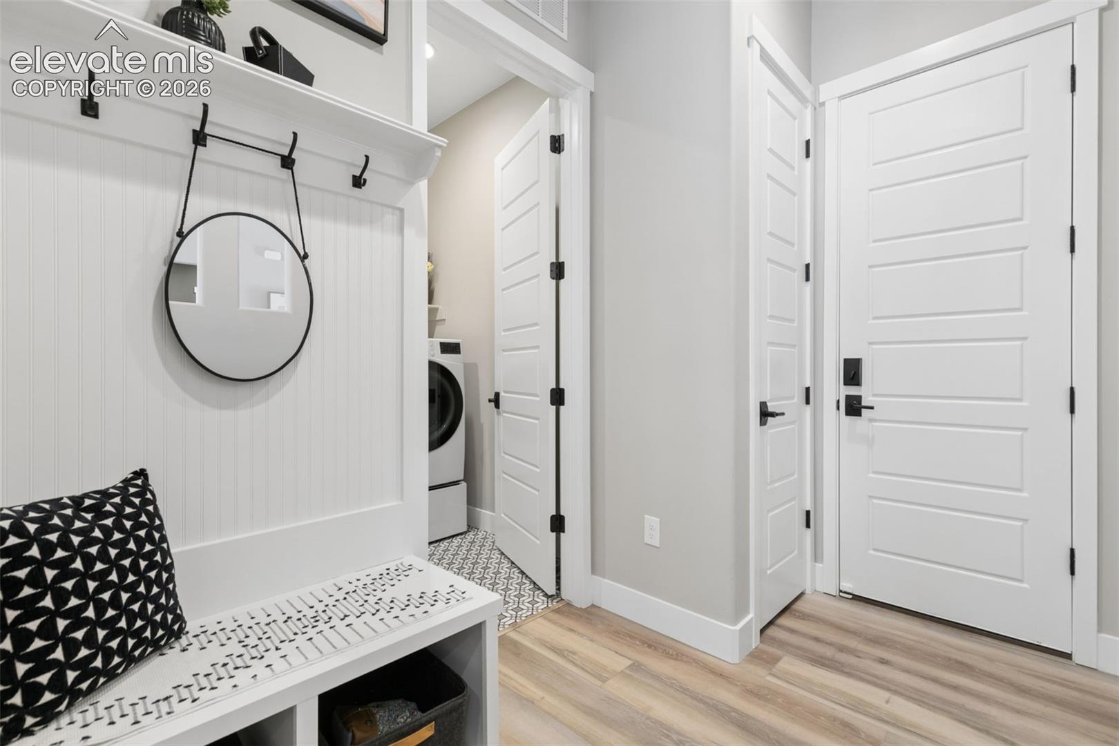 Mudroom entry with a built-in bench, round mirror, coat hooks, and laundry closet.