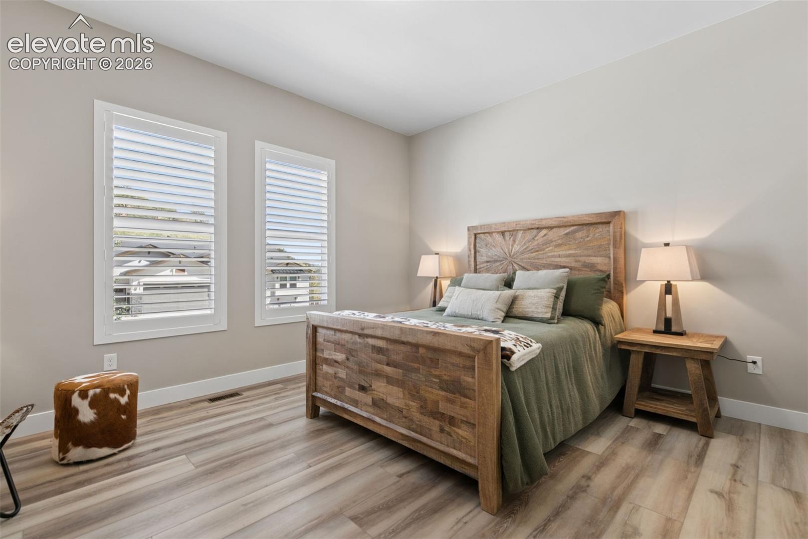 Staged bedroom with a rustic wooden bed, green bedding, and two shuttered windows.