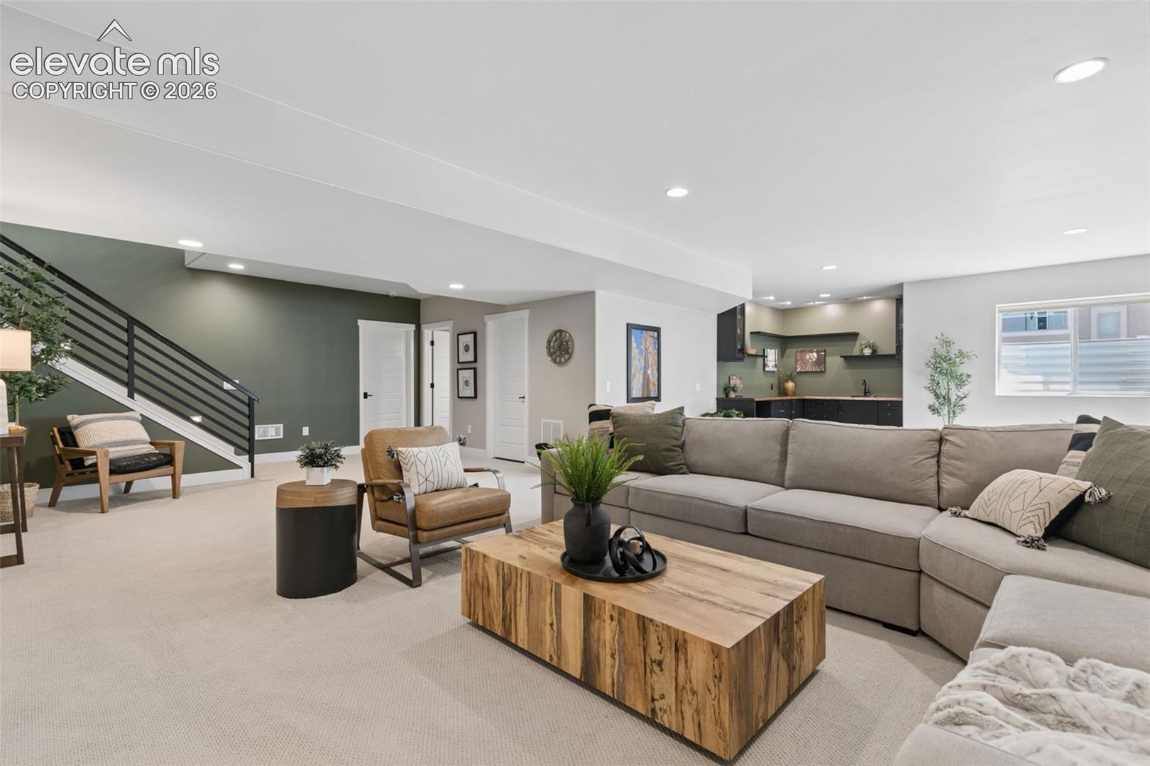 Living room with a large sectional, wood coffee table, and staircase beside a dark green accent wall.