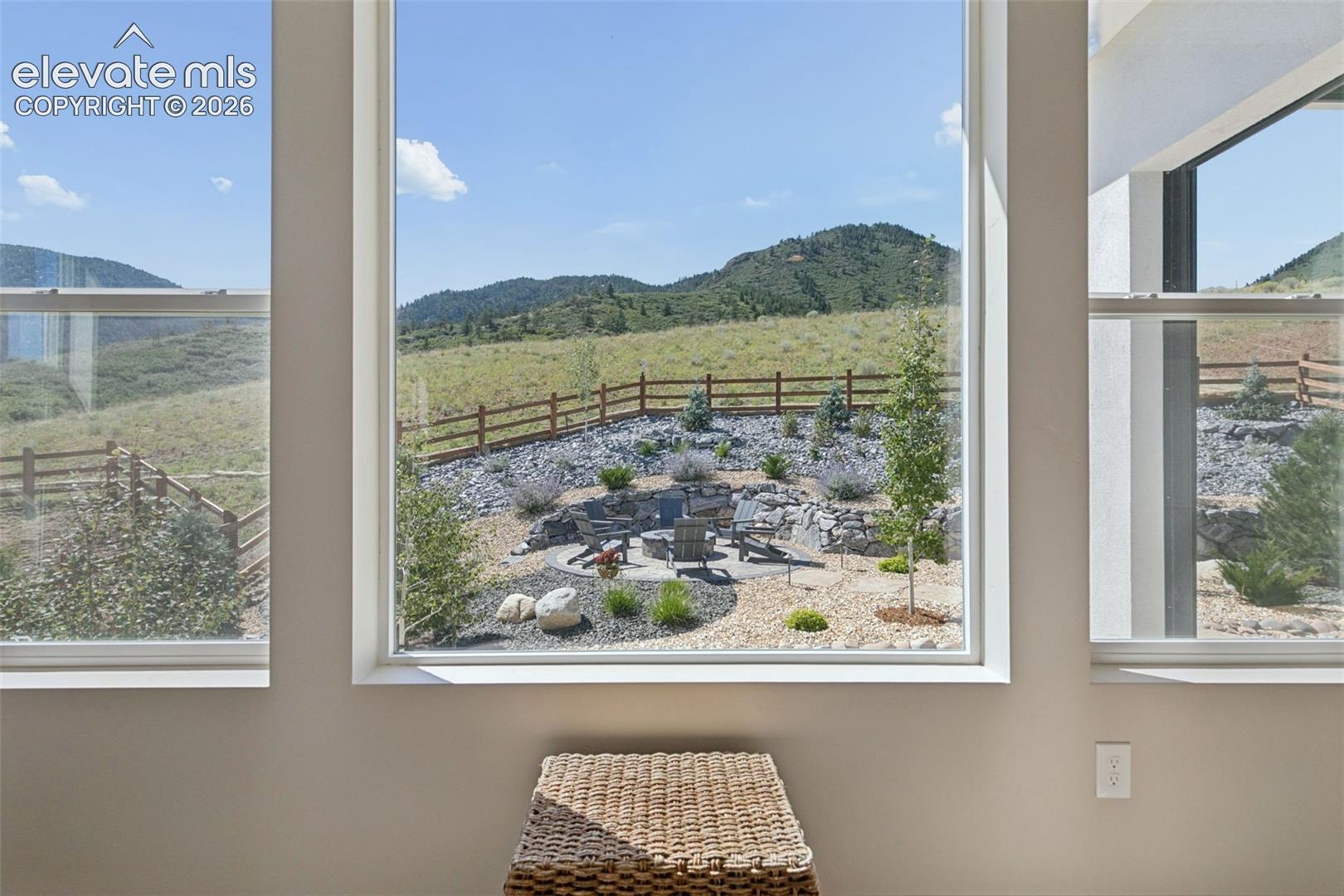 Large windows overlook a rocky fire-pit patio and green mountain hills.