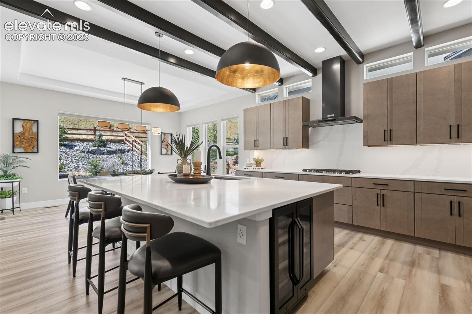 Modern kitchen with a large white island, taupe cabinets, and exposed dark ceiling beams.
