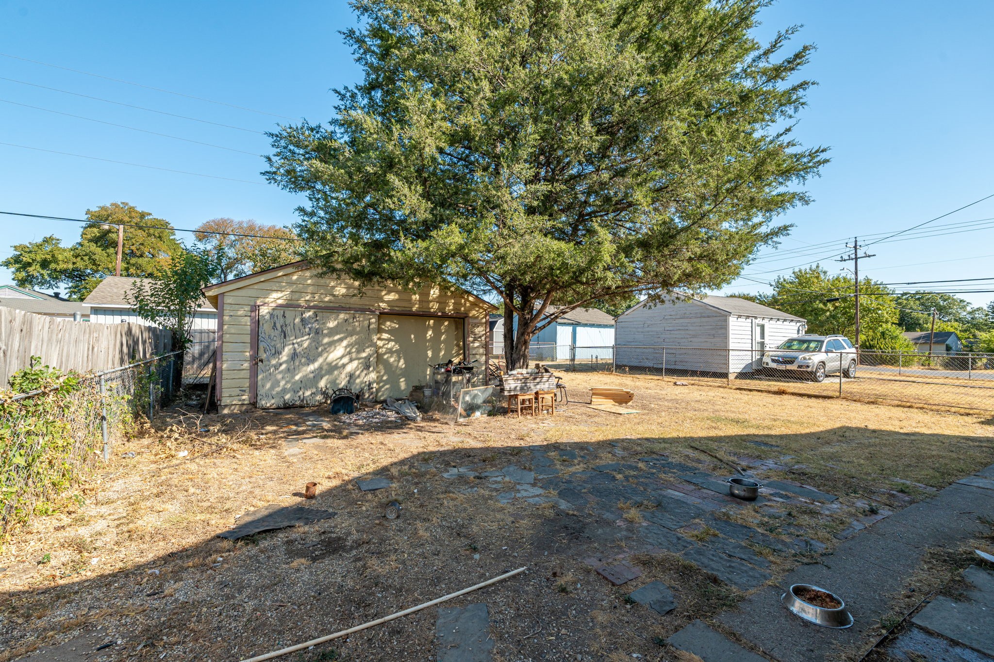 Backyard with a large shade tree over a detached garage and dry, patchy ground.