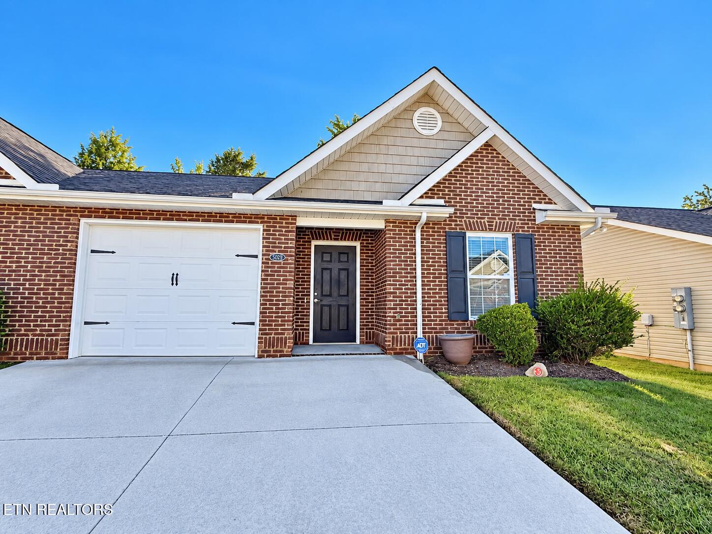 Brick house with a white double garage door, black shutters, and a wide concrete driveway.
