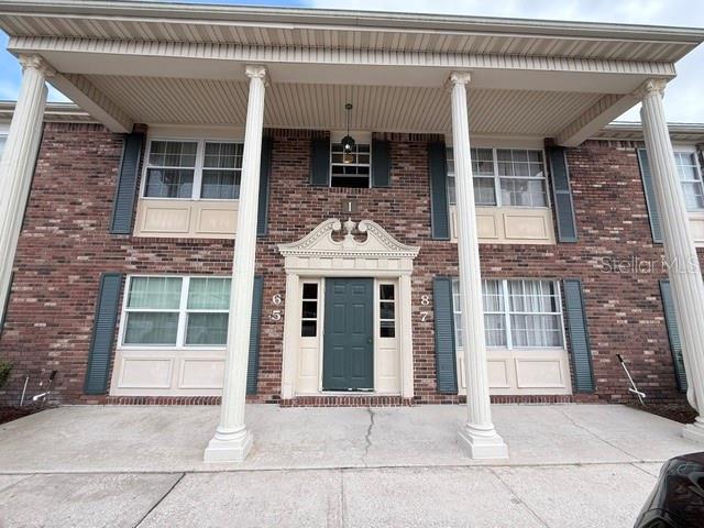 Brick residential building with a columned porch and dark green front door.