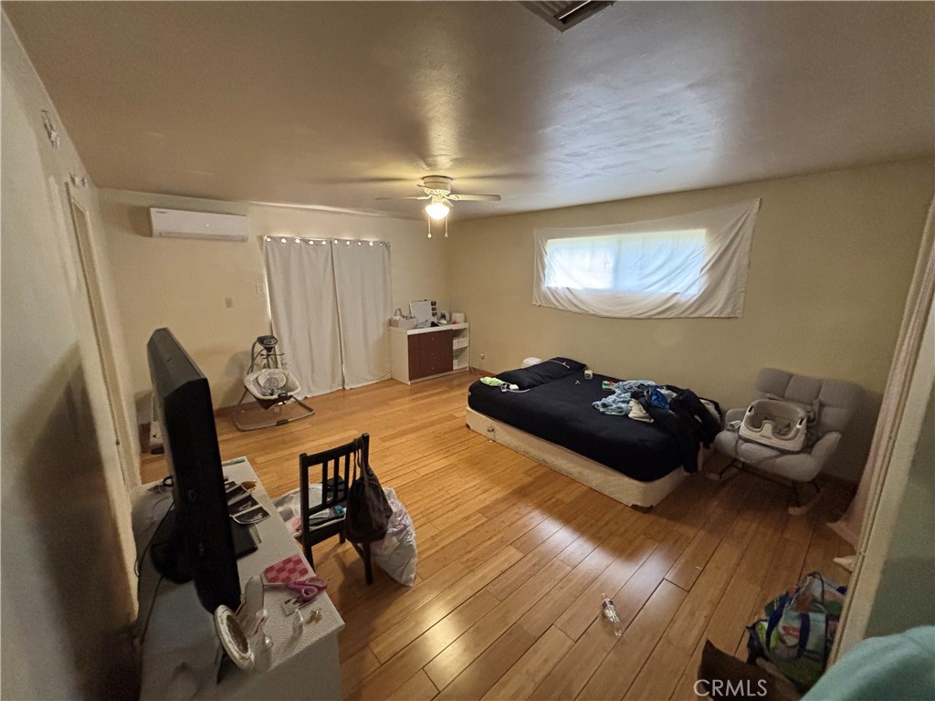 Bedroom with hardwood floors, a low bed, ceiling fan, and wall-mounted air conditioner.