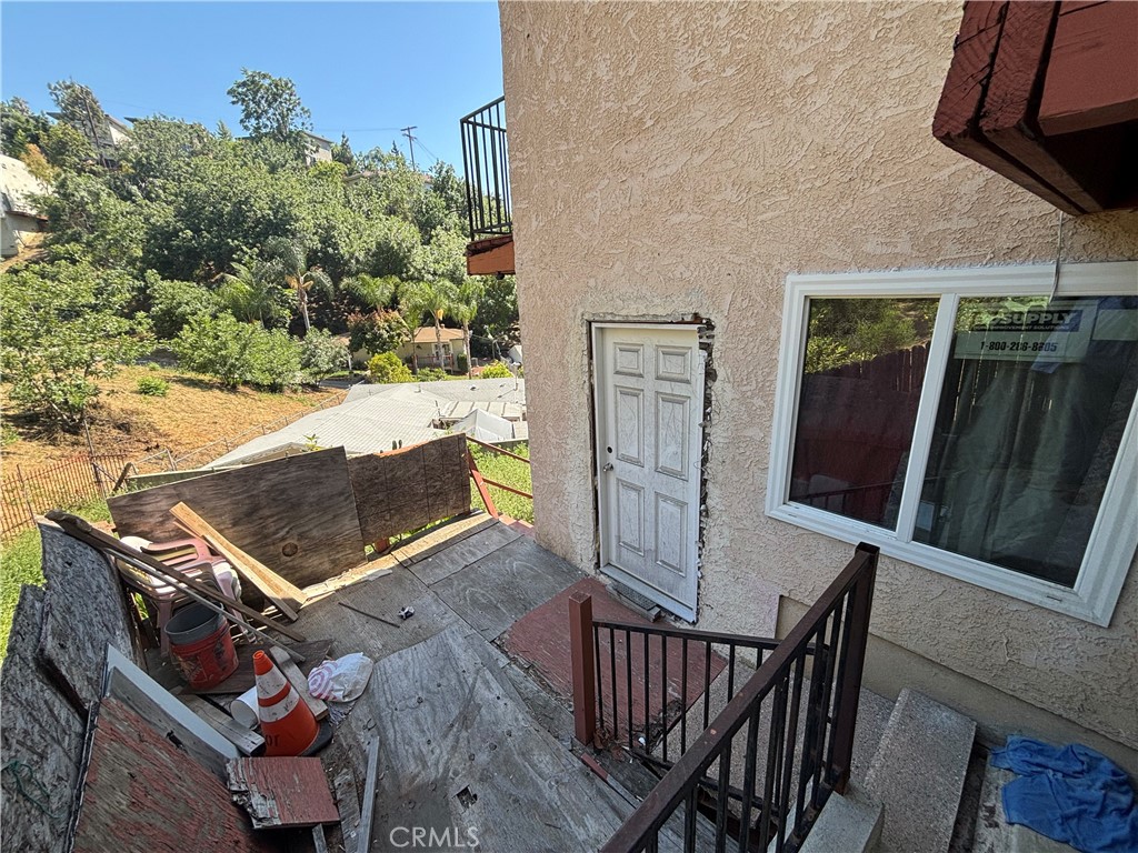 Stucco house entrance with a white door and a debris-strewn landing beside a wooded hillside.