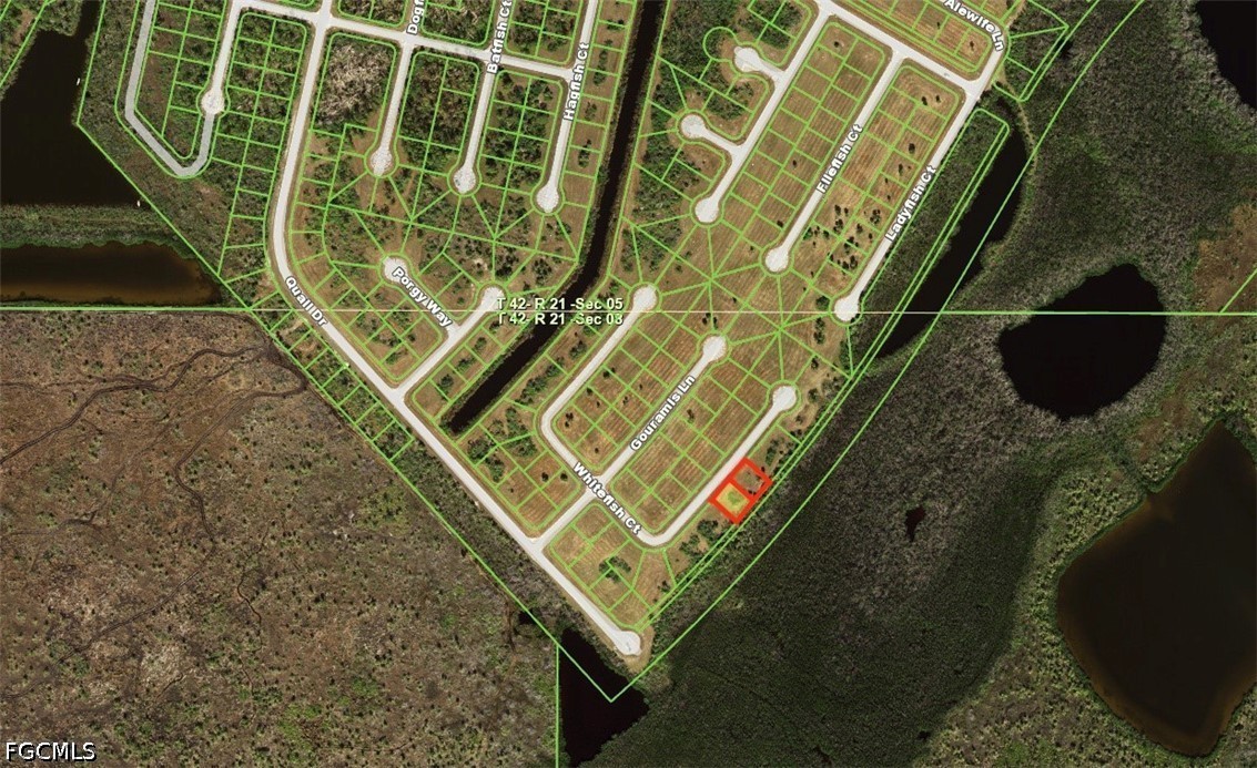 Aerial view of a vacant lot outlined in red beside a subdivision and surrounding wetlands.