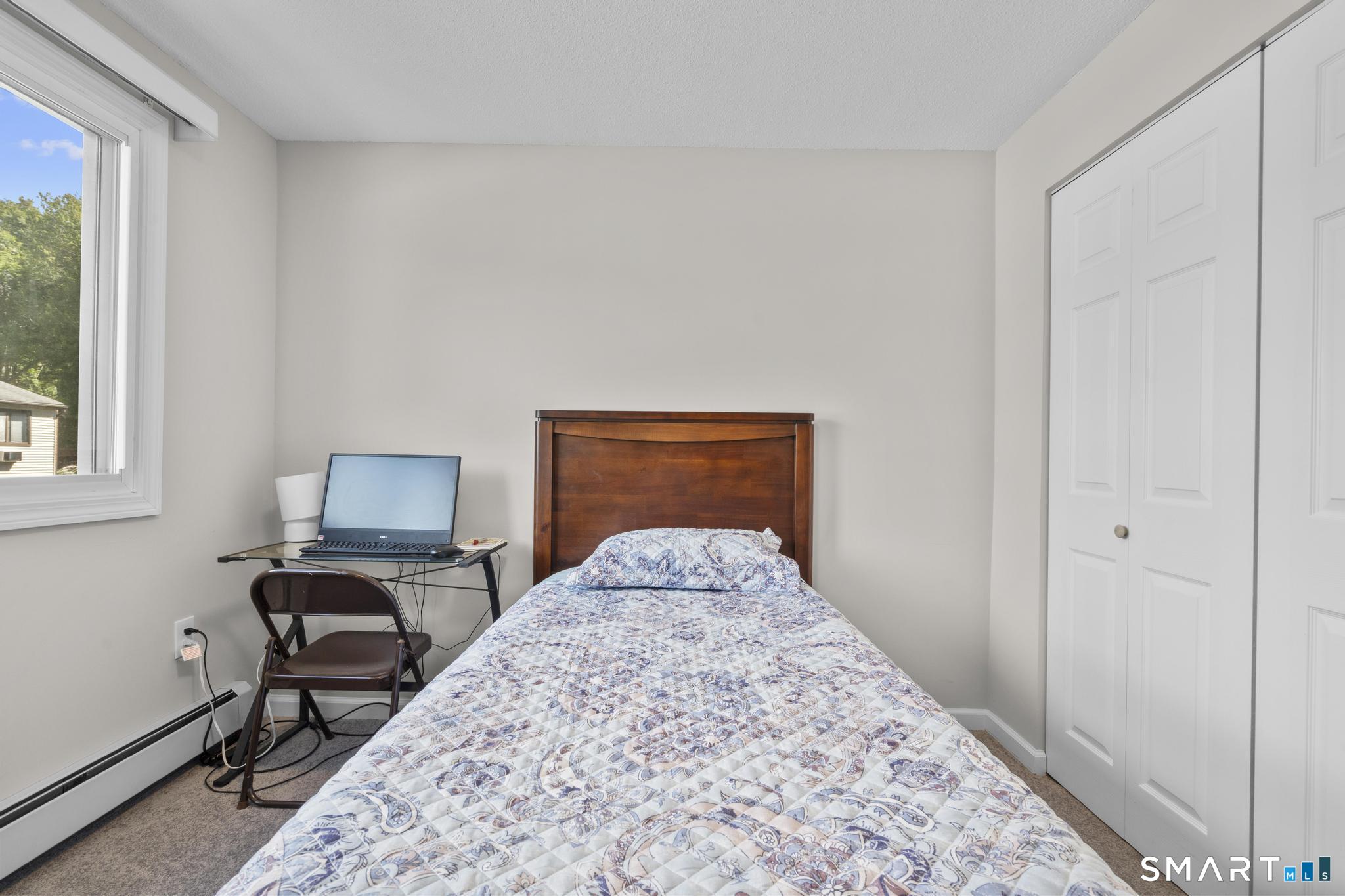 Bedroom with a single bed, wooden headboard, window, and laptop on a folding desk.