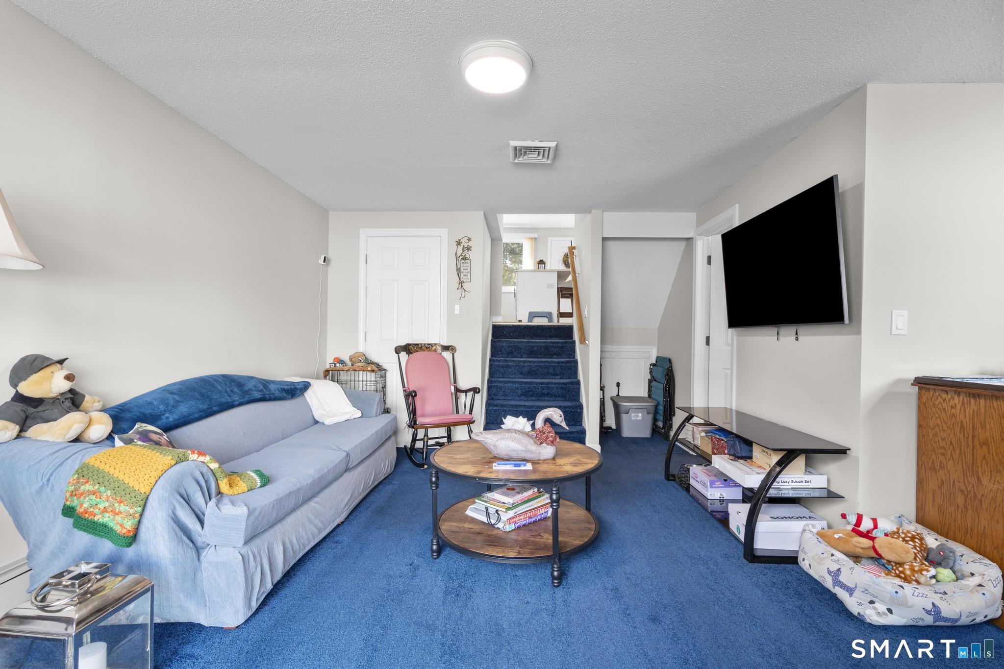 Furnished living room with blue carpet, a sofa, and stairs leading to the upper level.