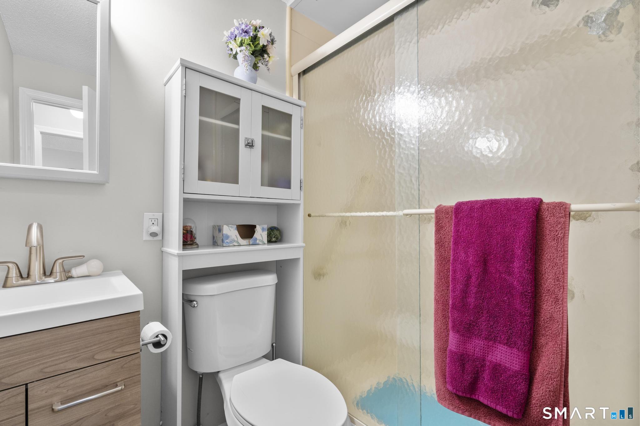 Bathroom with a glass shower, wood vanity, and white storage cabinet above the toilet.