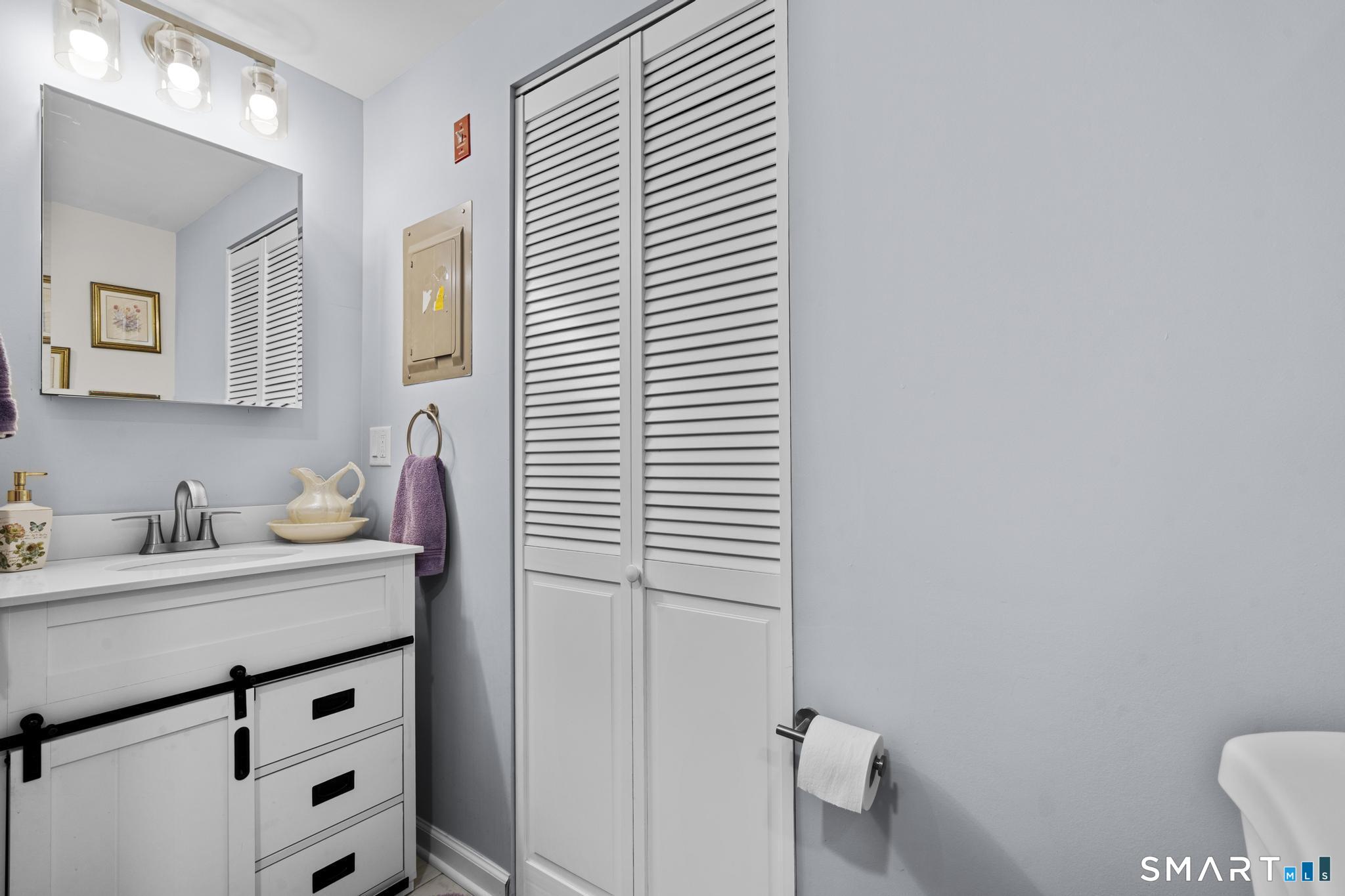 Bathroom with a white vanity, mirrored cabinet, and louvered closet doors.