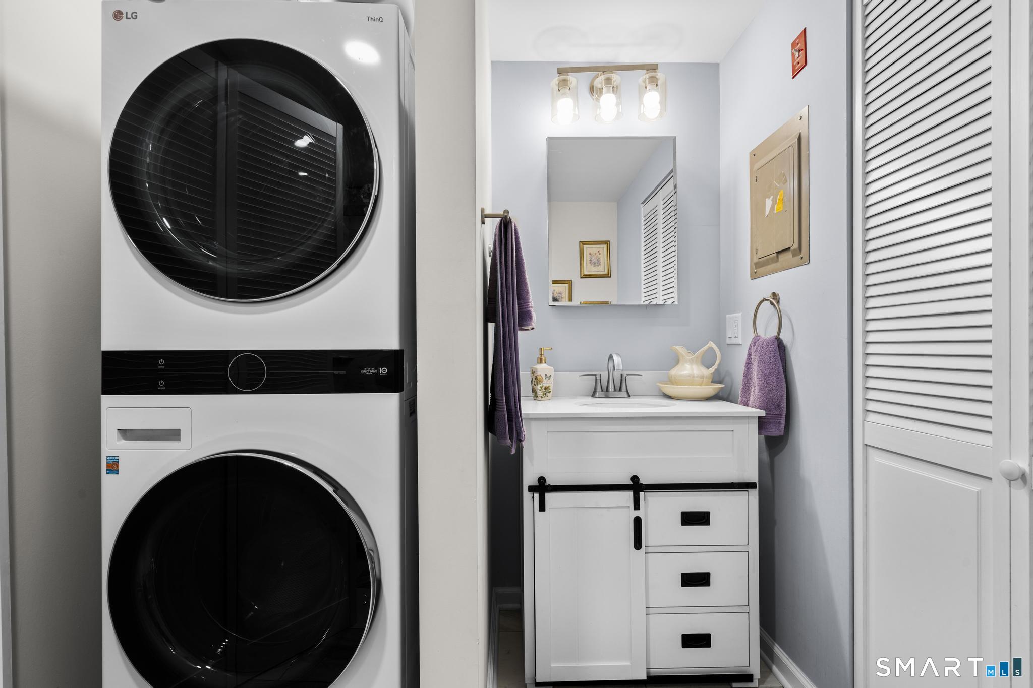 Laundry area with stacked washer and dryer beside a white vanity and mirror.