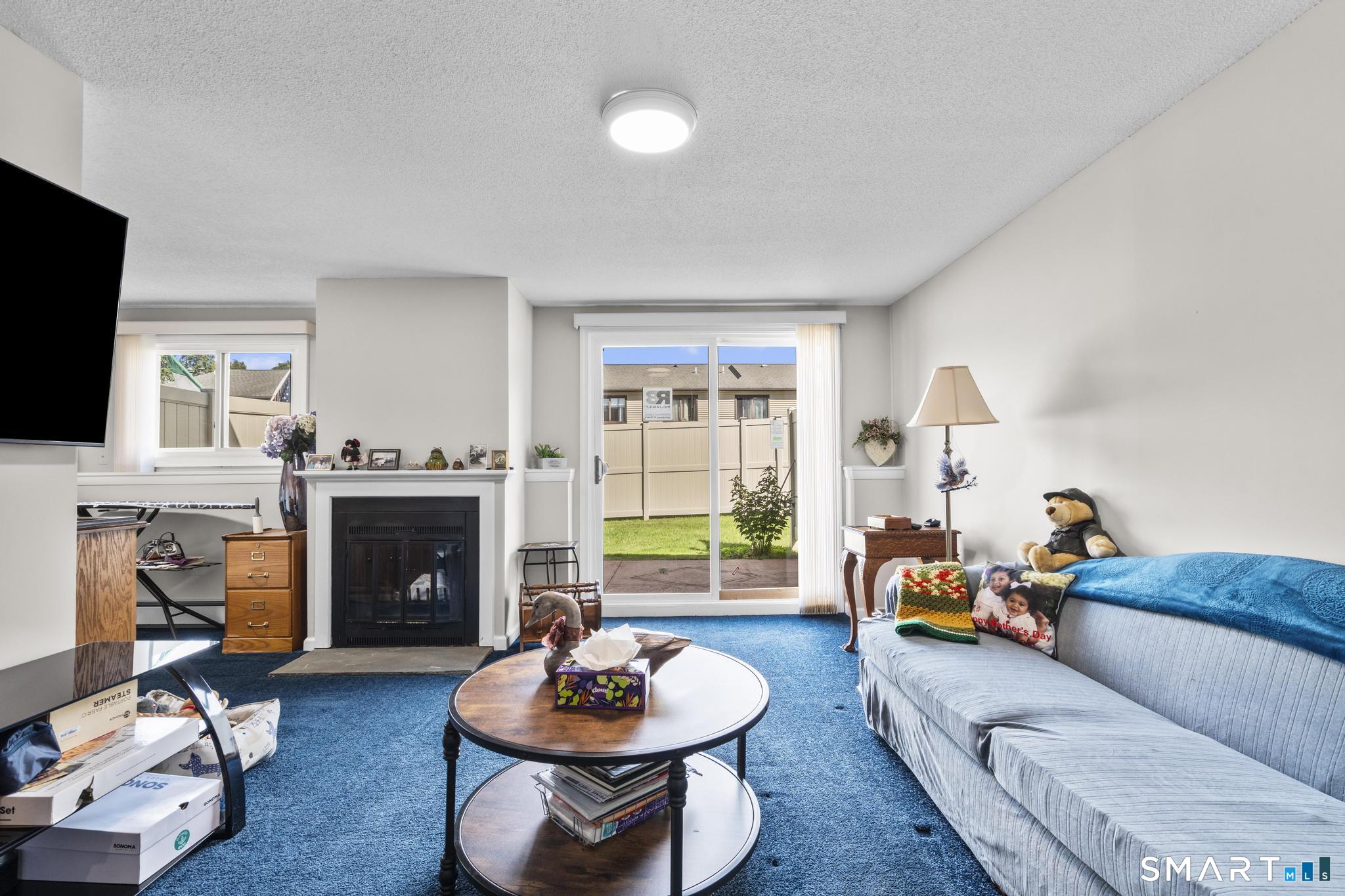 Living room with blue carpet, a fireplace, sliding glass doors, and a long sofa.