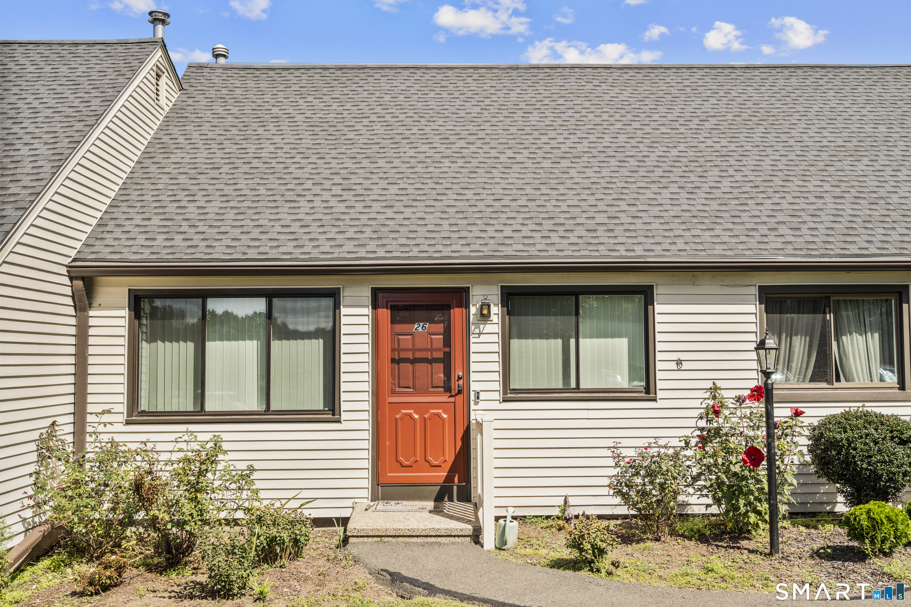 Home exterior with a red entry door, wide windows, and landscaped front walkway.
