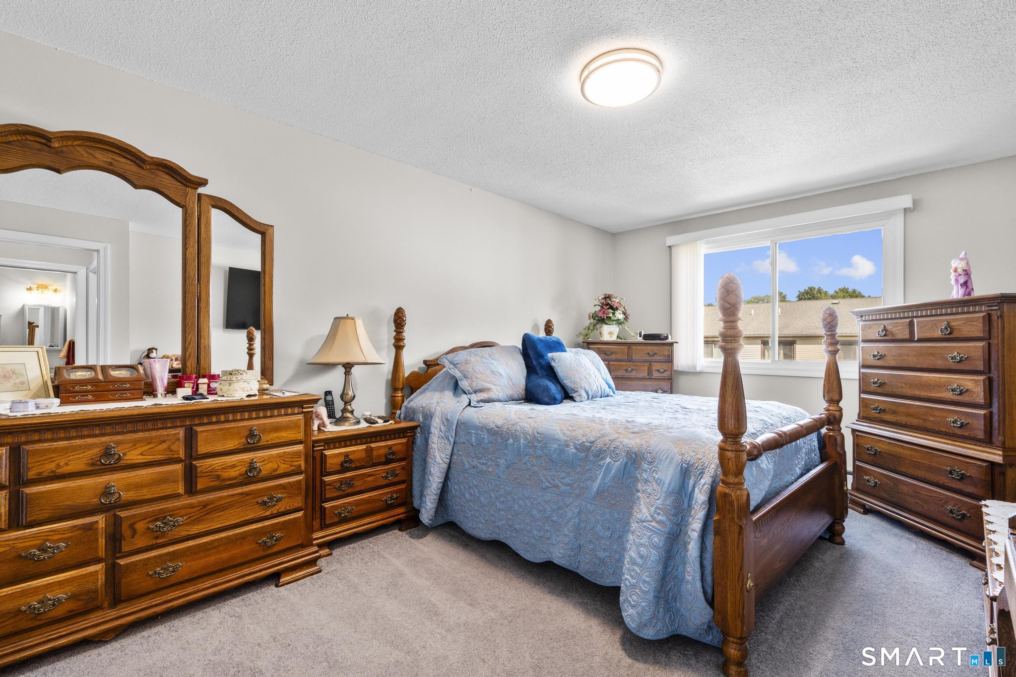 Bedroom with a blue quilted bed, ornate wooden furniture, and a large window.