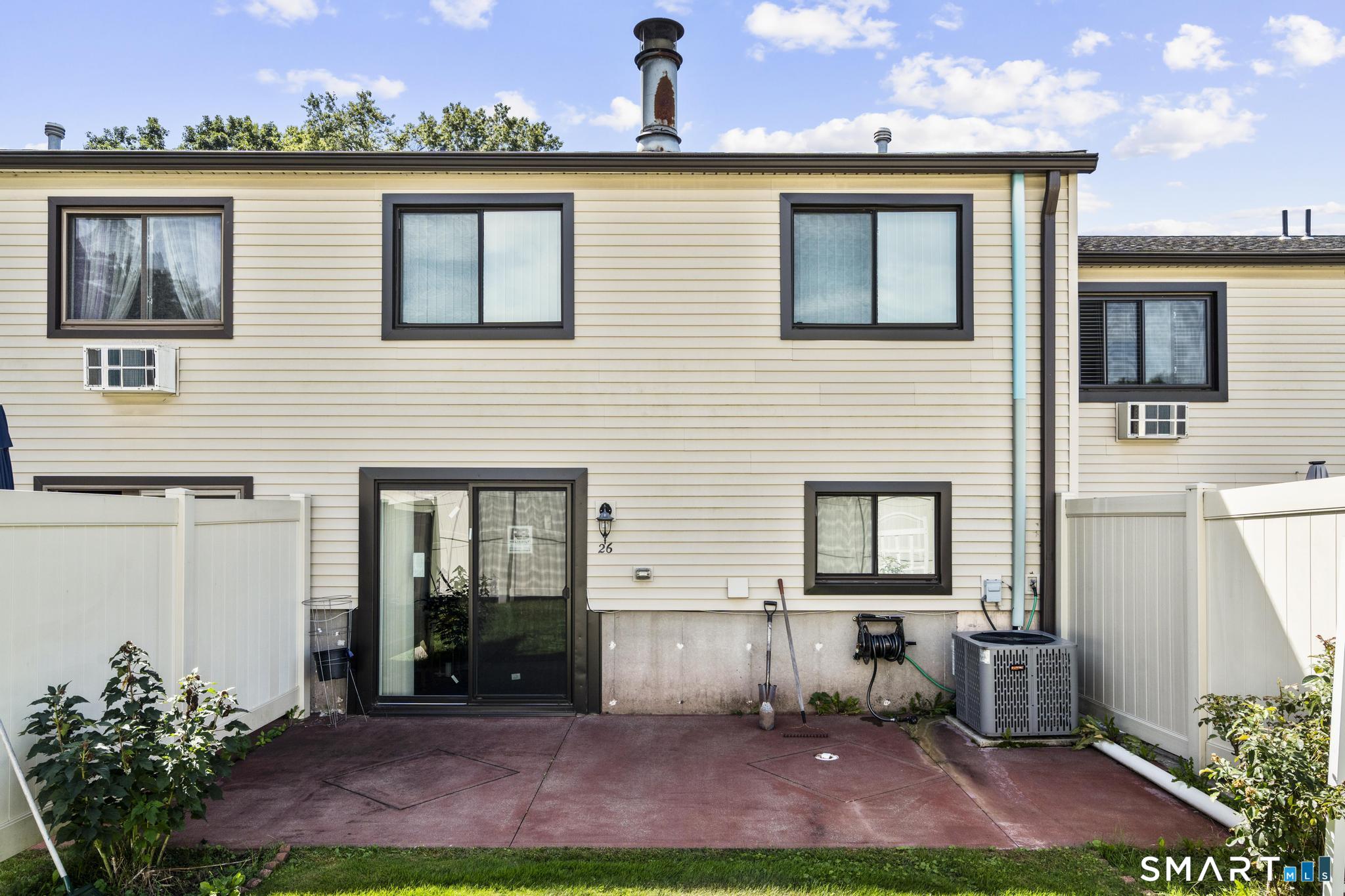 Rear of a townhouse with a fenced concrete patio, sliding glass door, and outdoor air-conditioning unit.