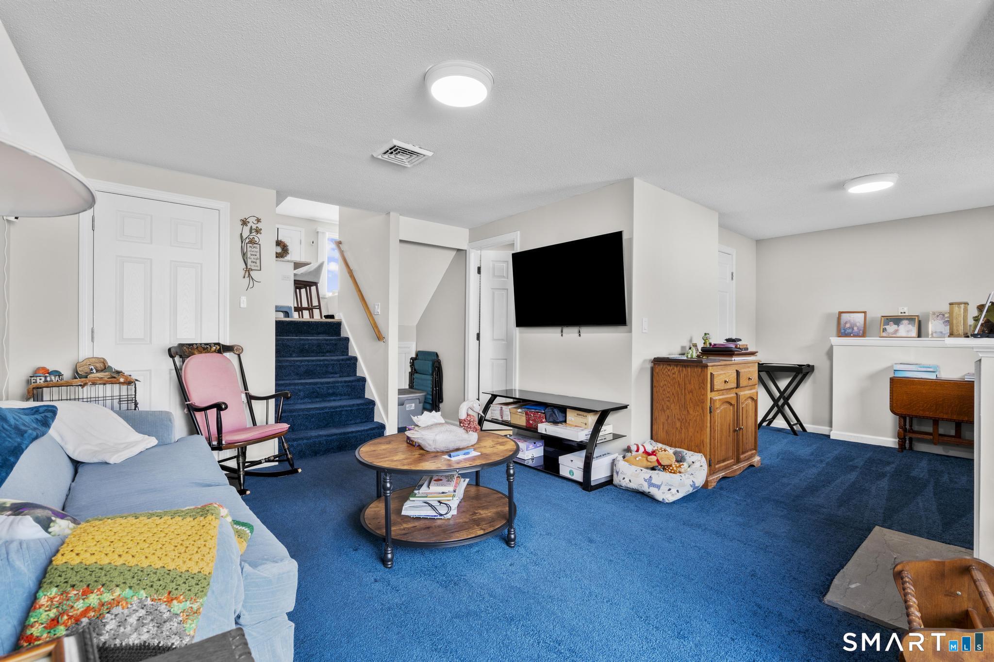 Furnished living room with bright blue carpet, a staircase, and a wall-mounted television.