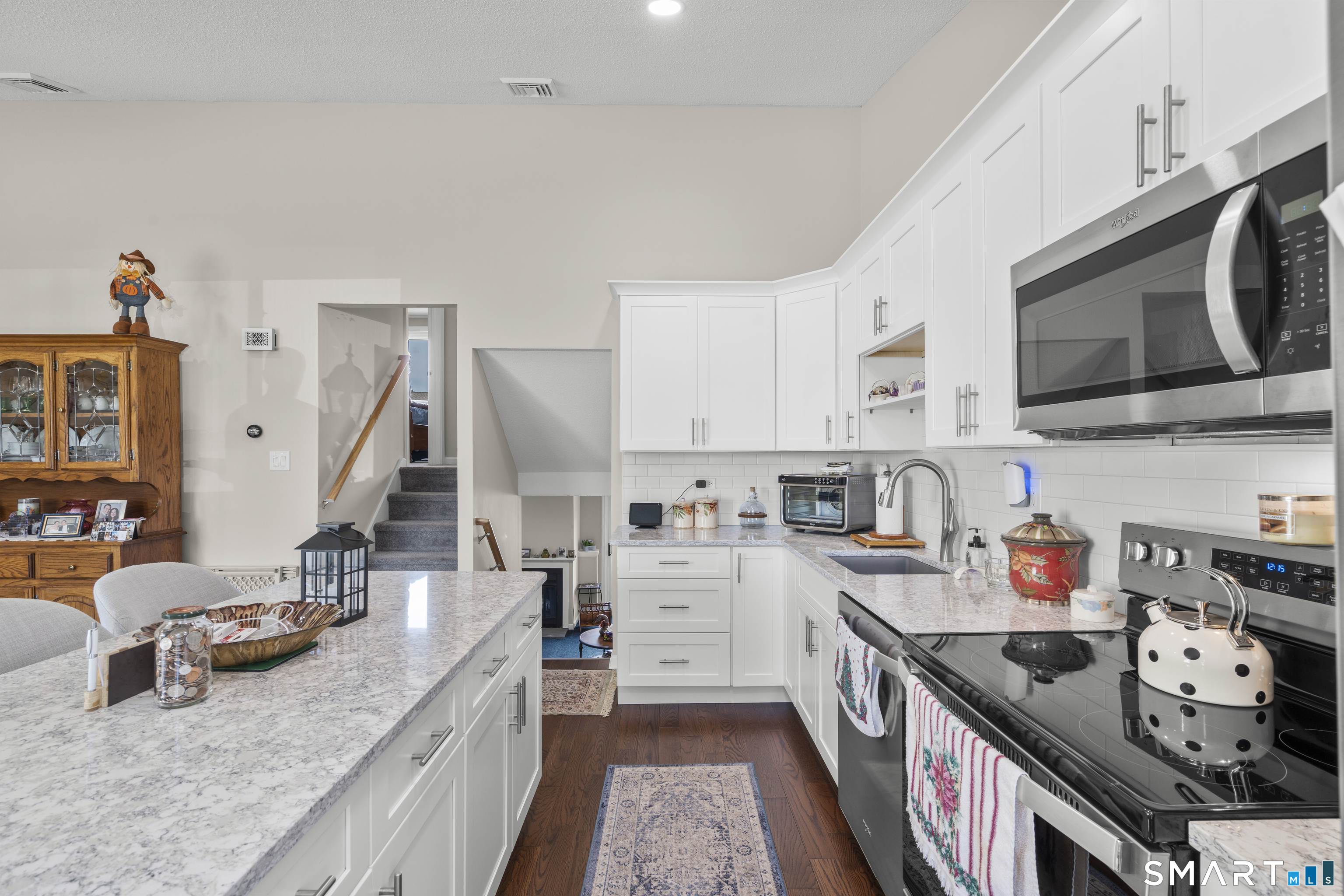 Kitchen with white cabinets, marble-pattern counters, stainless appliances, and a long central island.