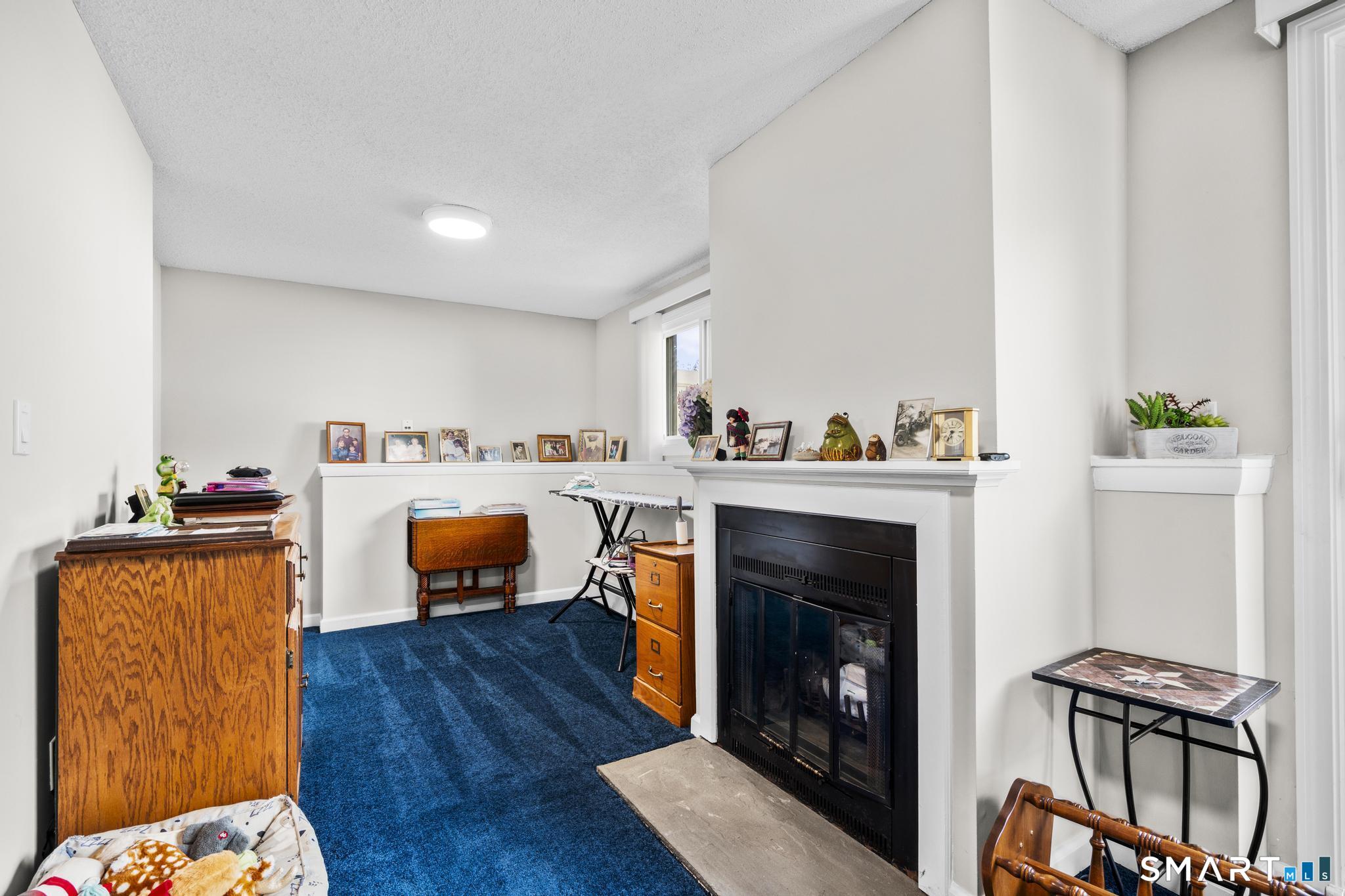 Furnished living room with a black fireplace, white mantel, and blue carpet.