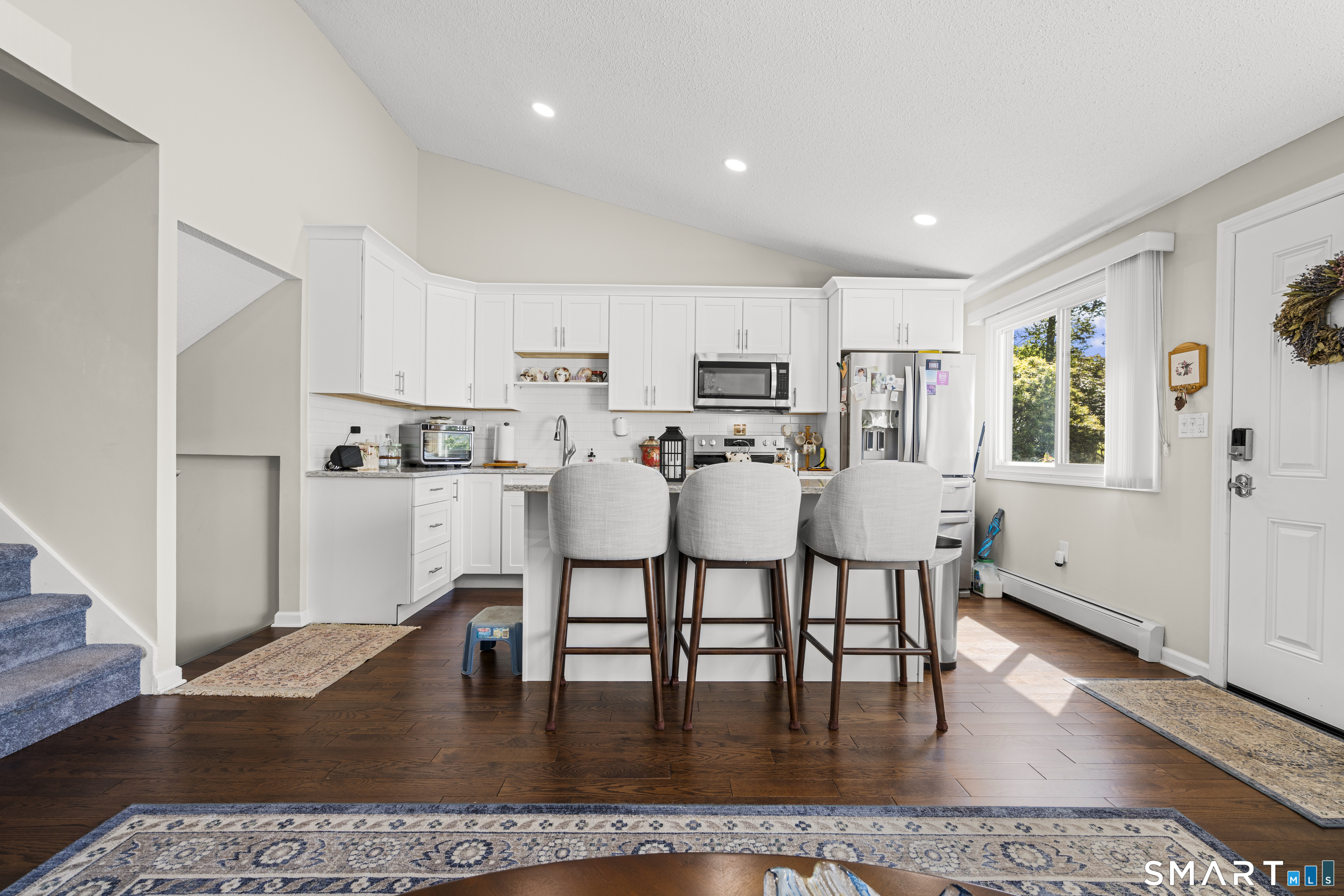 Bright kitchen with white cabinetry, island seating, stainless appliances, and dark hardwood floors.