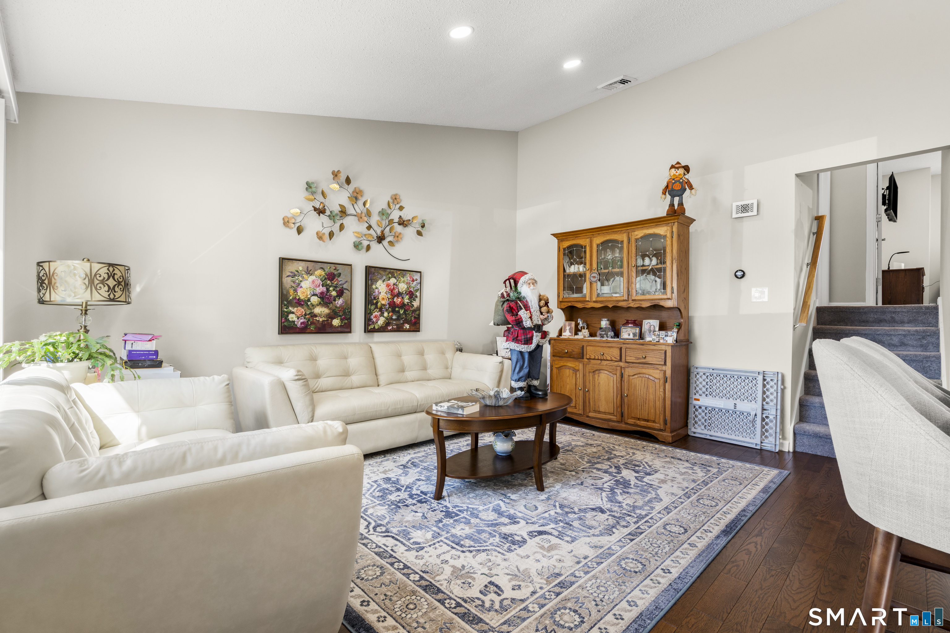Furnished living room with cream sofas, a wooden display cabinet, and patterned area rug.