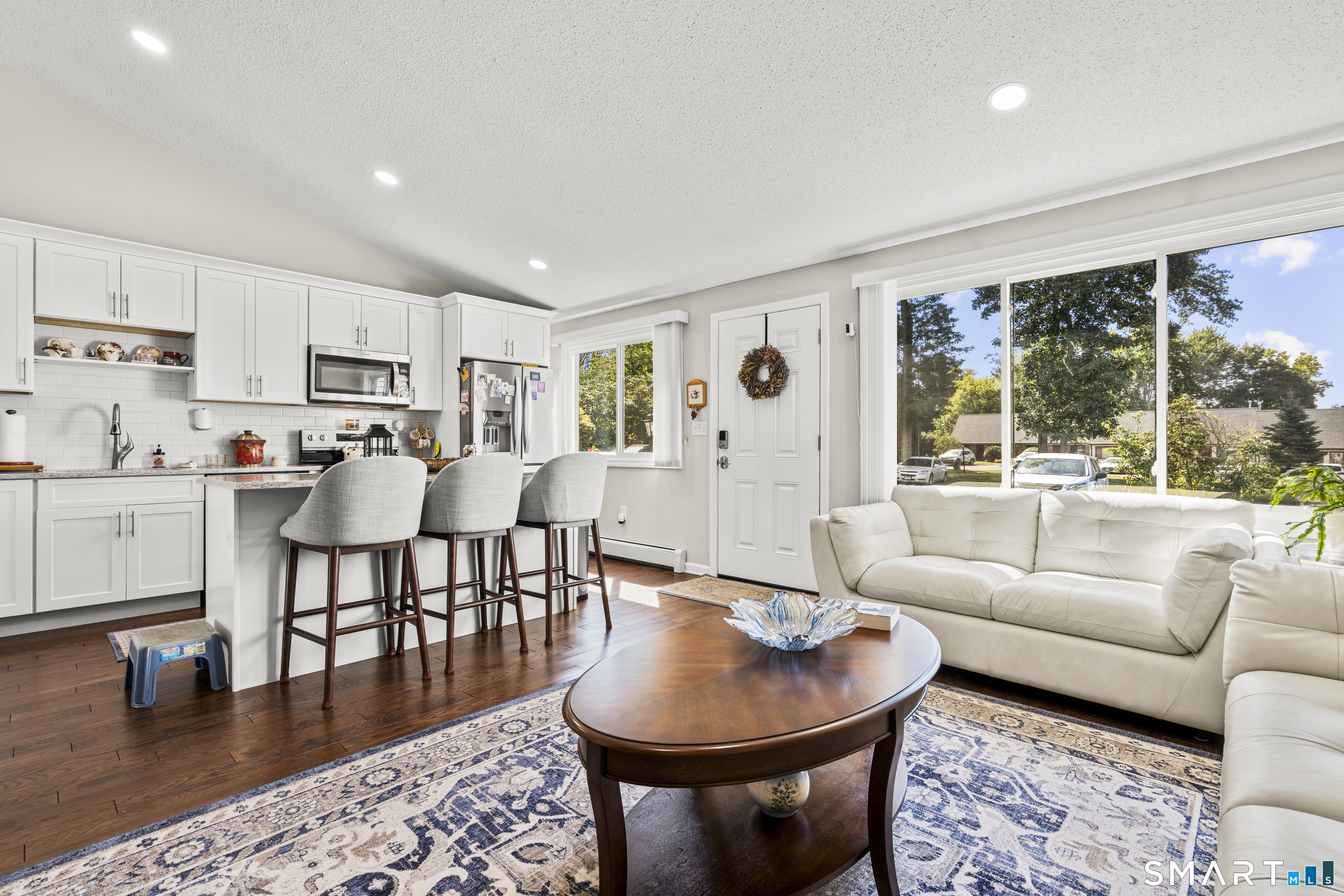 Open-plan living room and kitchen with a white sofa, island seating, and large windows.