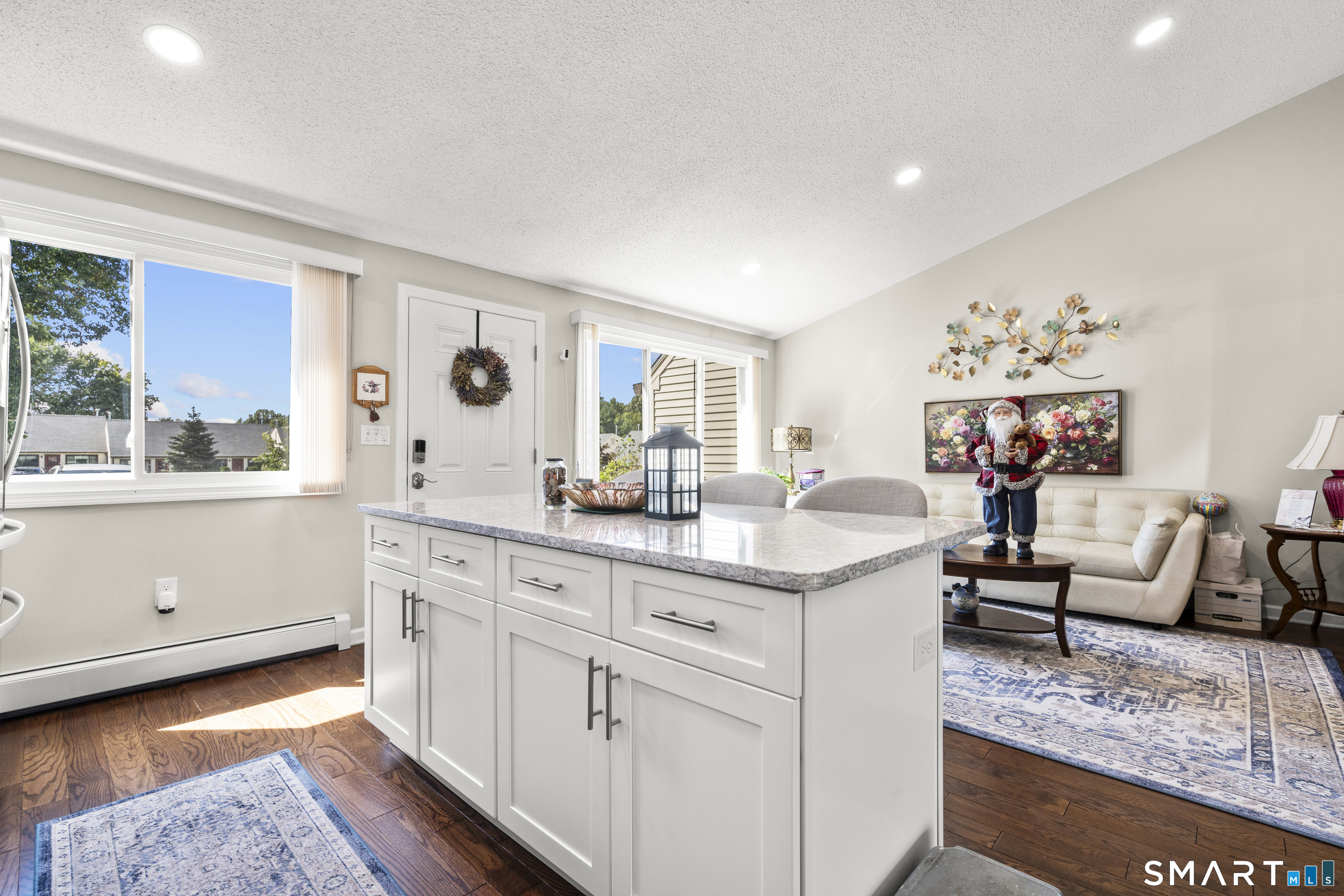 Bright kitchen with a large white island, opening into a furnished living room.