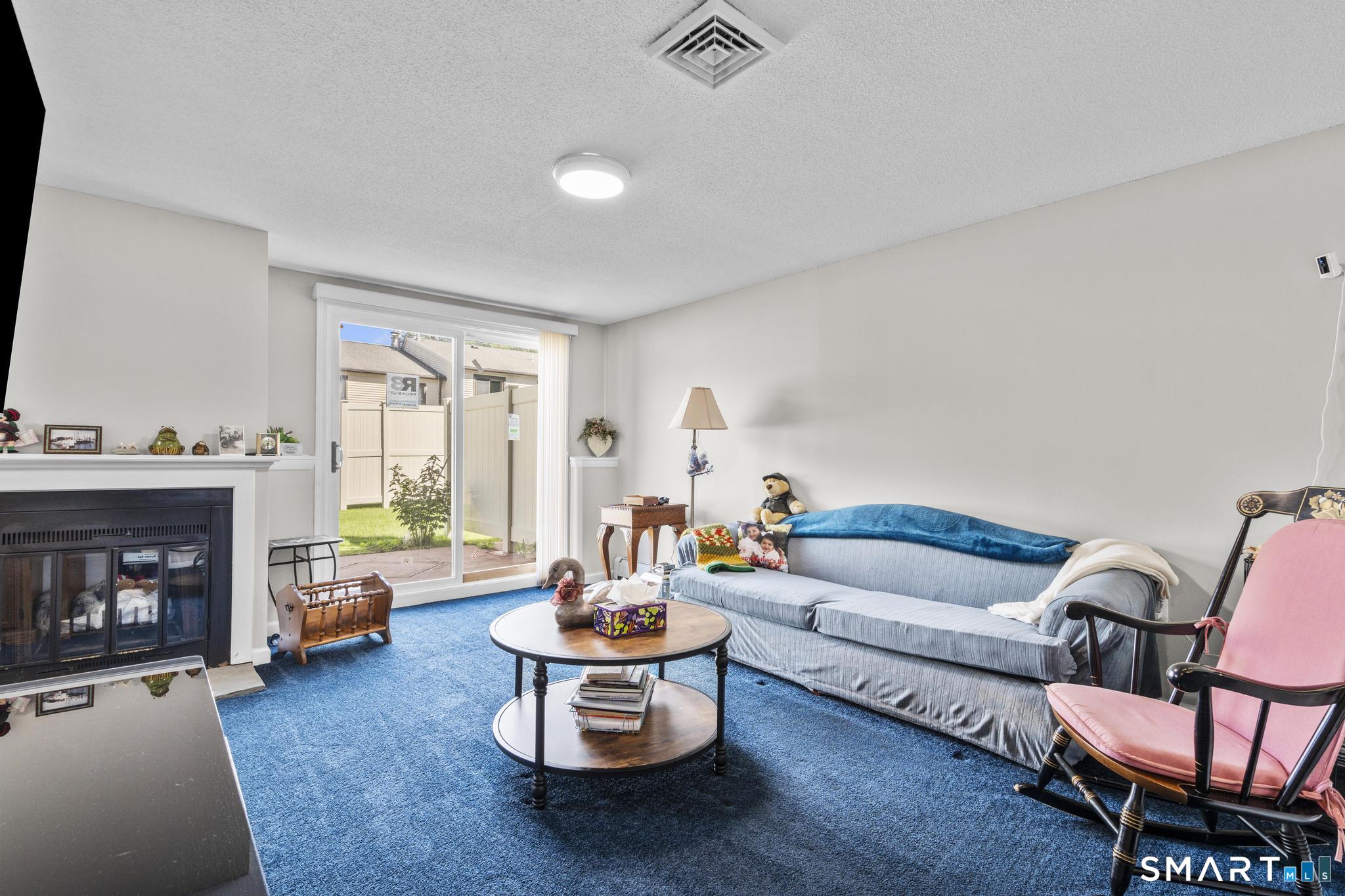 Living room with blue carpet, a fireplace, and a sliding glass door beside a sofa.
