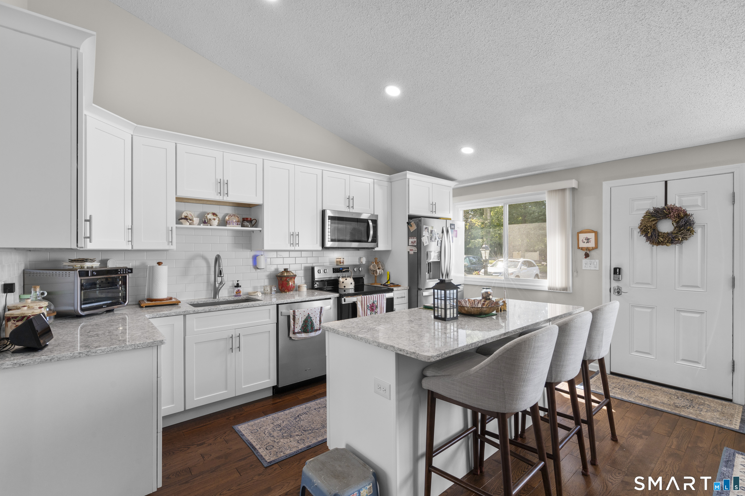 Bright kitchen with white cabinets, a large granite island, stainless appliances, and bar seating.