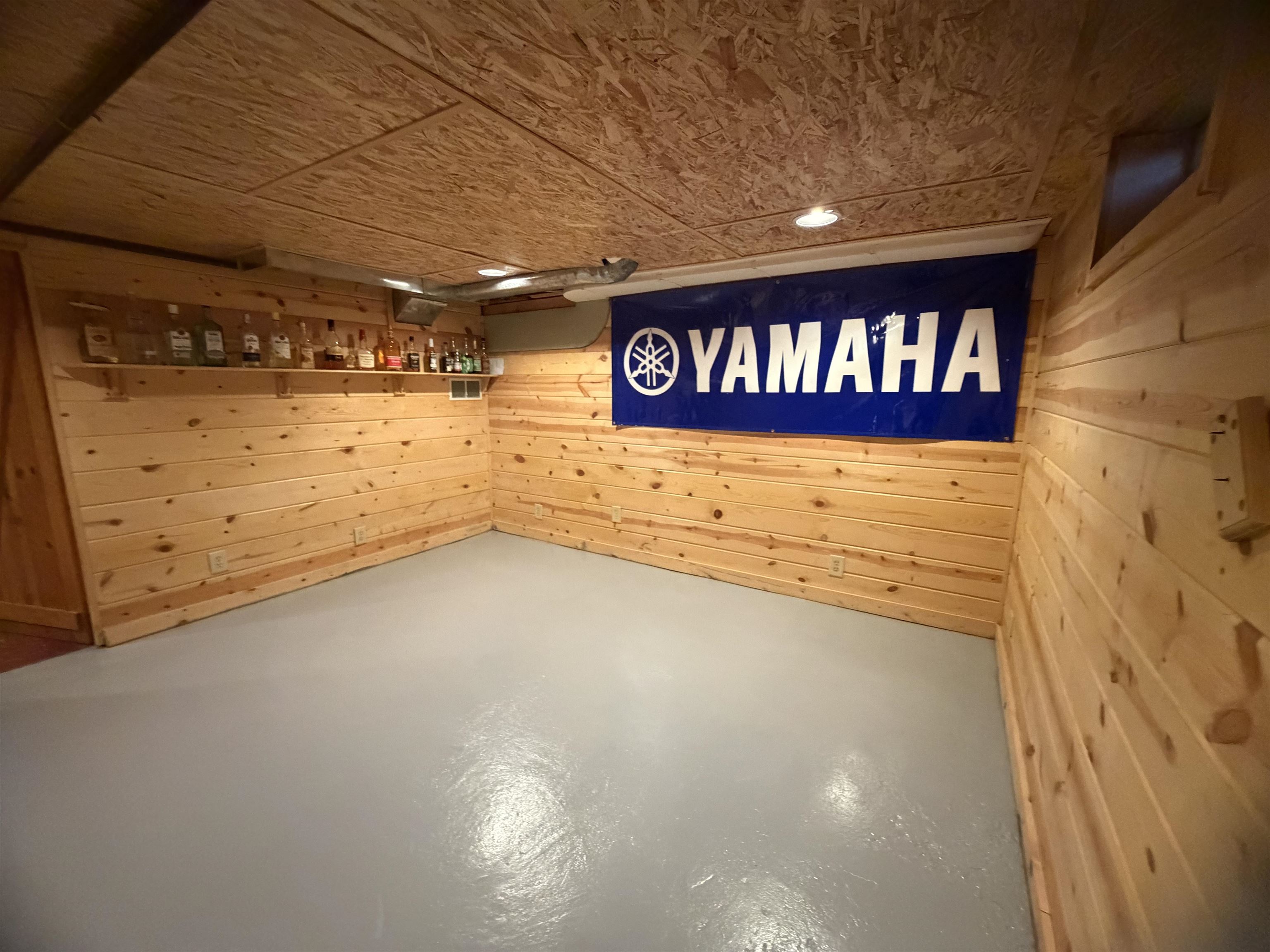 Wood-paneled room with a gray floor, bottle shelf, and Yamaha banner.