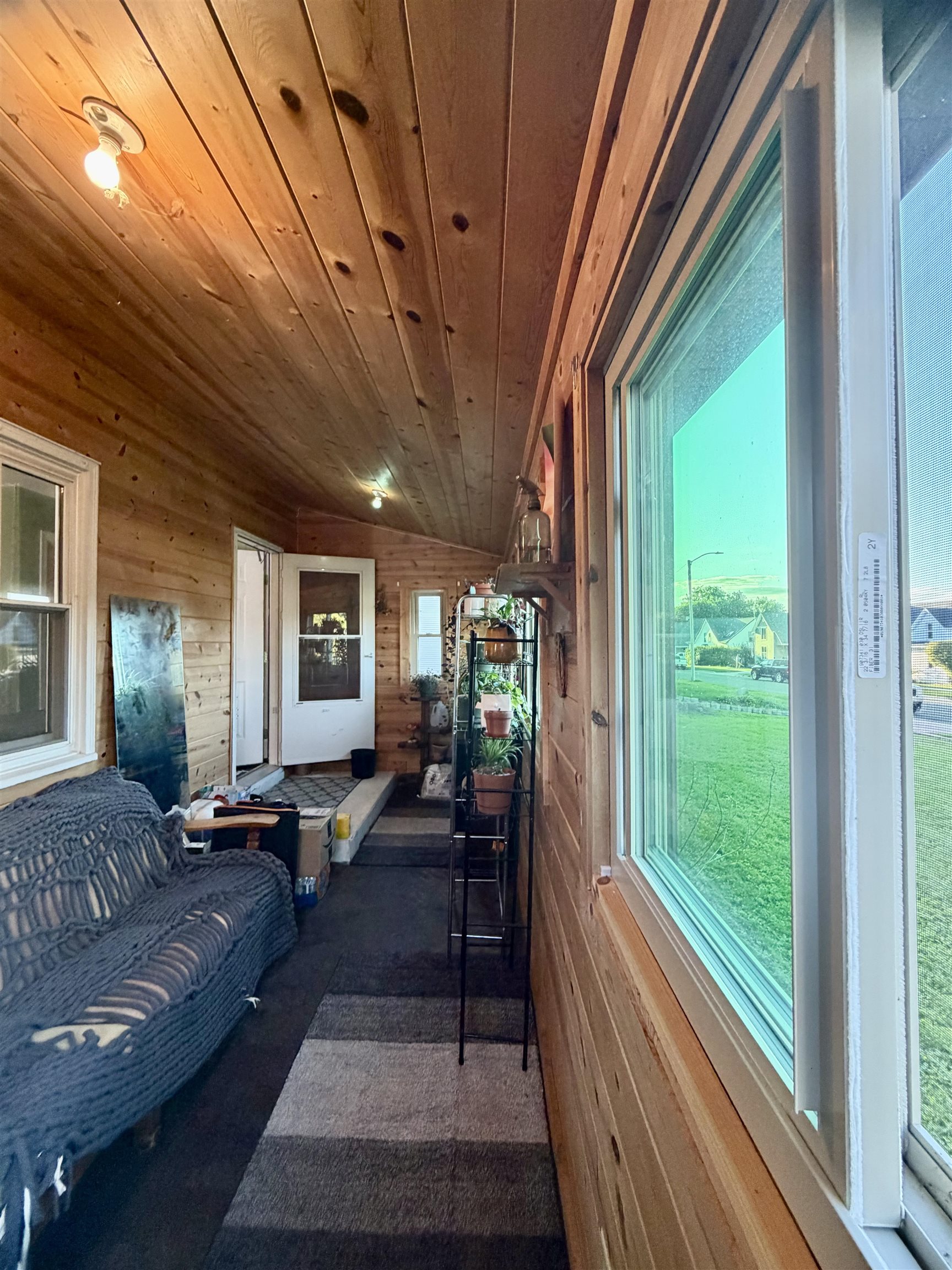 Wood-paneled sunroom with a gray sofa, potted plants, and large windows overlooking a lawn.