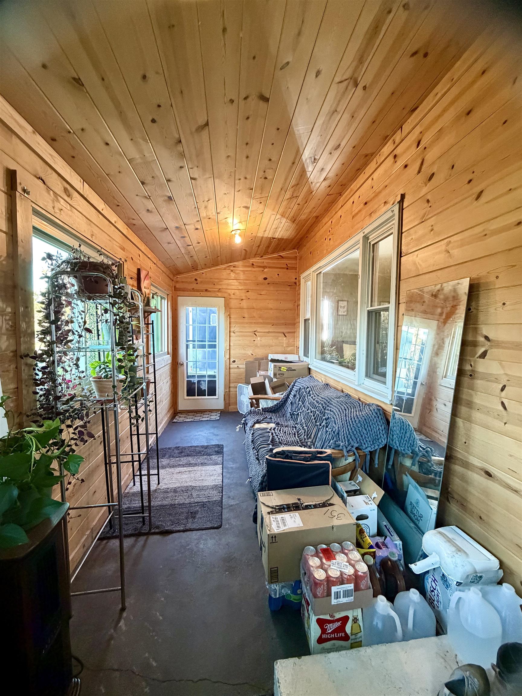 Enclosed wood-paneled porch with a plant shelf, couch, and boxes.